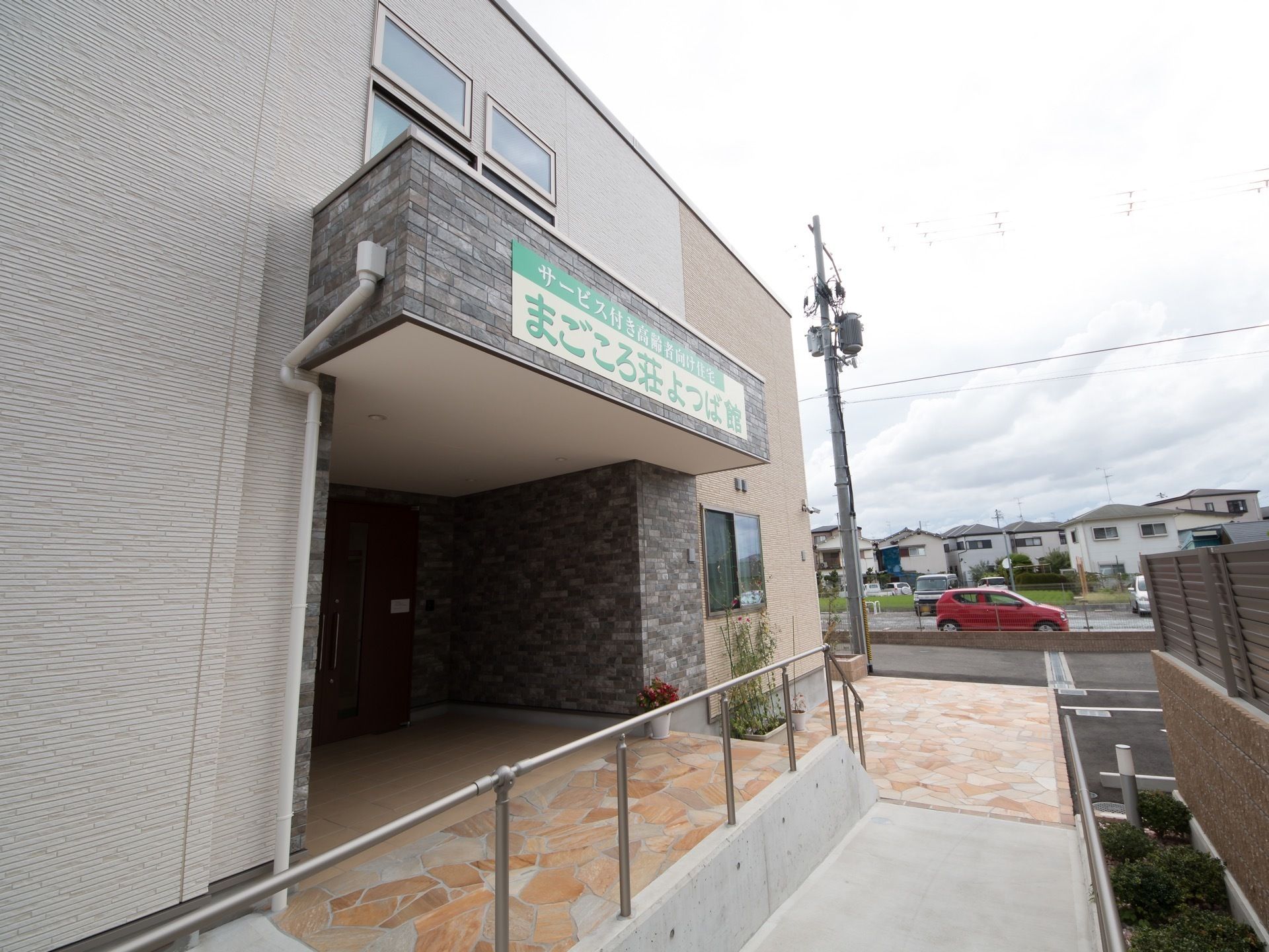 右側にはスロープが設置され、側には花壇が設けられている。建物の壁際には鉢などに植えられた花が置いてある。