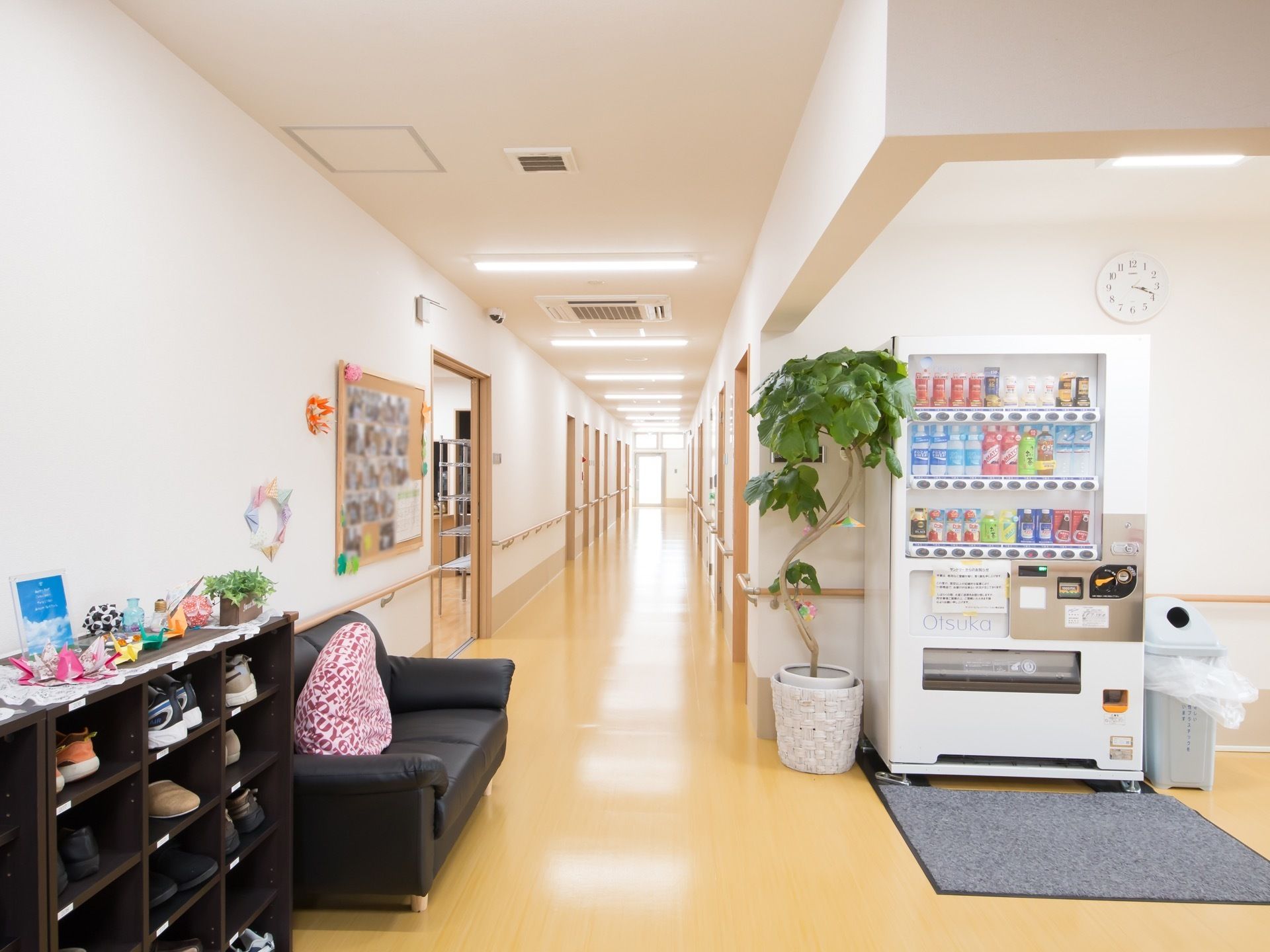 左側には靴箱やソファが置かれており、右側には自動販売機が設置されている。壁にはコルクボードや、折り紙で作った飾りが貼られている。