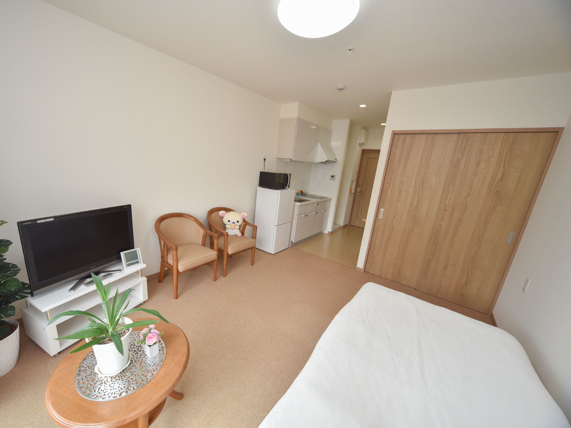 部屋には、キッチンがあり手元と足元には白い収納棚がついている。またテレビ台とベッド、冷蔵庫などもある。