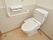 ベージュの床に白でまとめたトイレスペース。トイレットホルダーは2つ。安全面に考慮し手すりや呼び出しブザーも設置している。