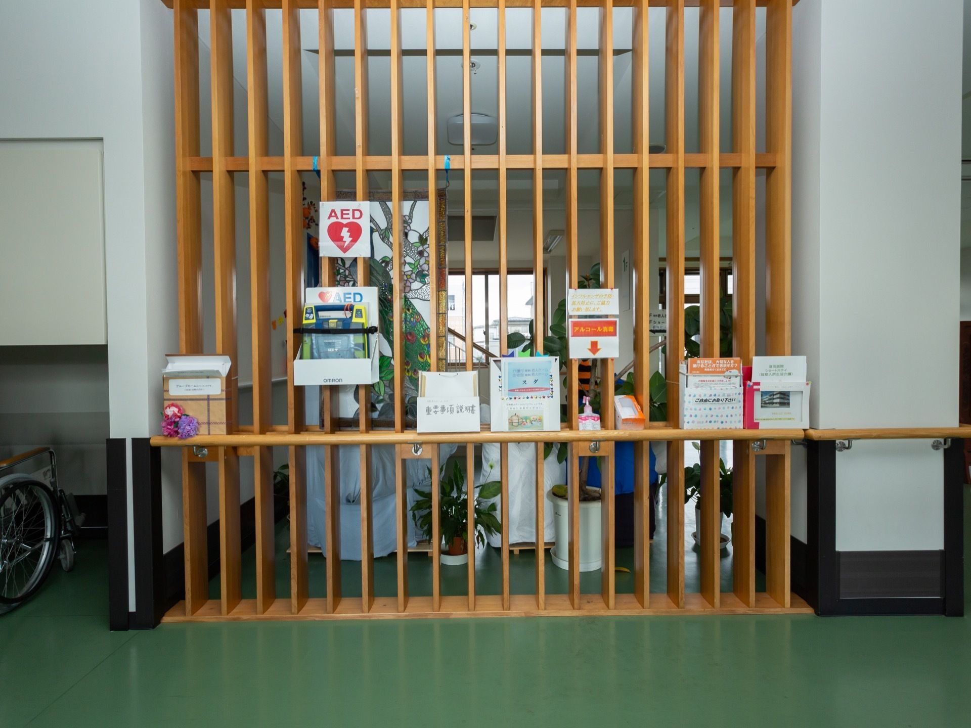 廊下の一部分に木製の格子があり、施設やAEDのパンフレット、説明書などが置かれている。アルコール消毒液もある。