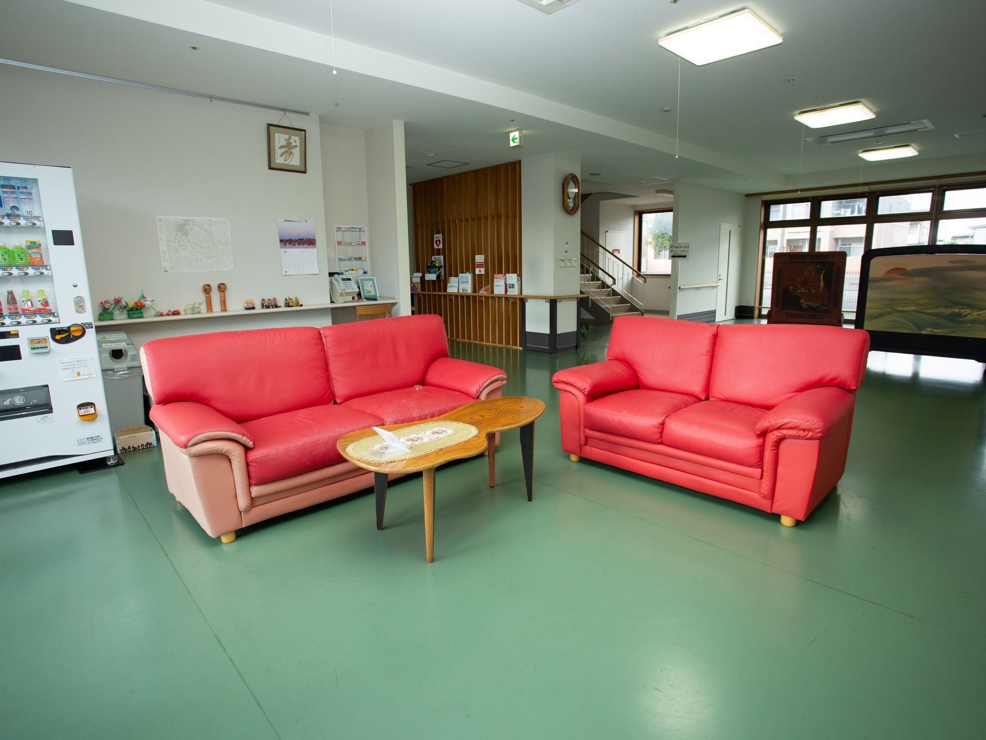 廊下の一角のオープンスペースに２台の赤い大型ソファとテーブルがある。すぐそばに、飲み物の自動販売機が設置されている。