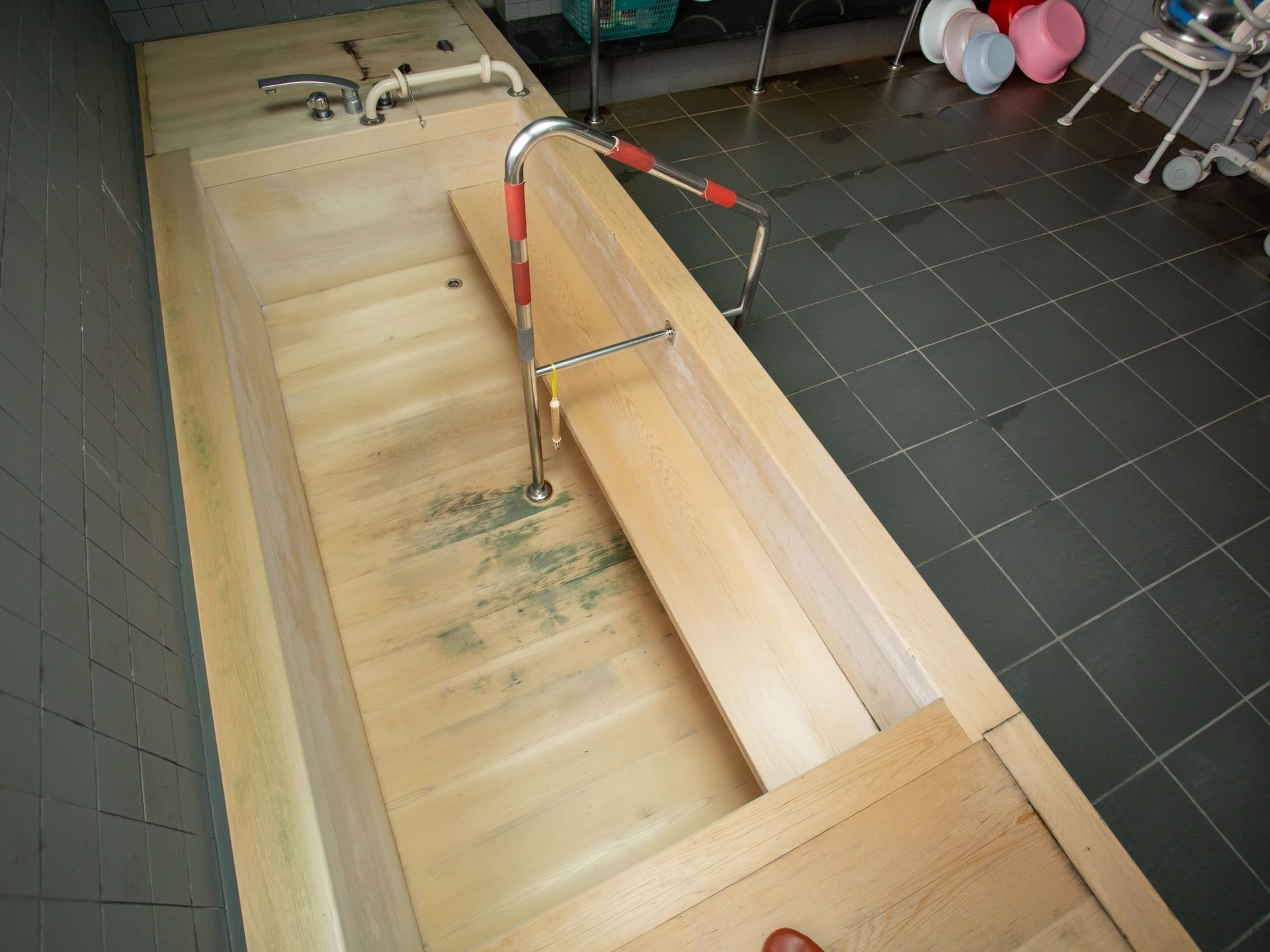 グレーのタイル張りの浴室に、木製の浴槽がある。浴槽には出入りしやすいよう、手すりや階段が備わっている。