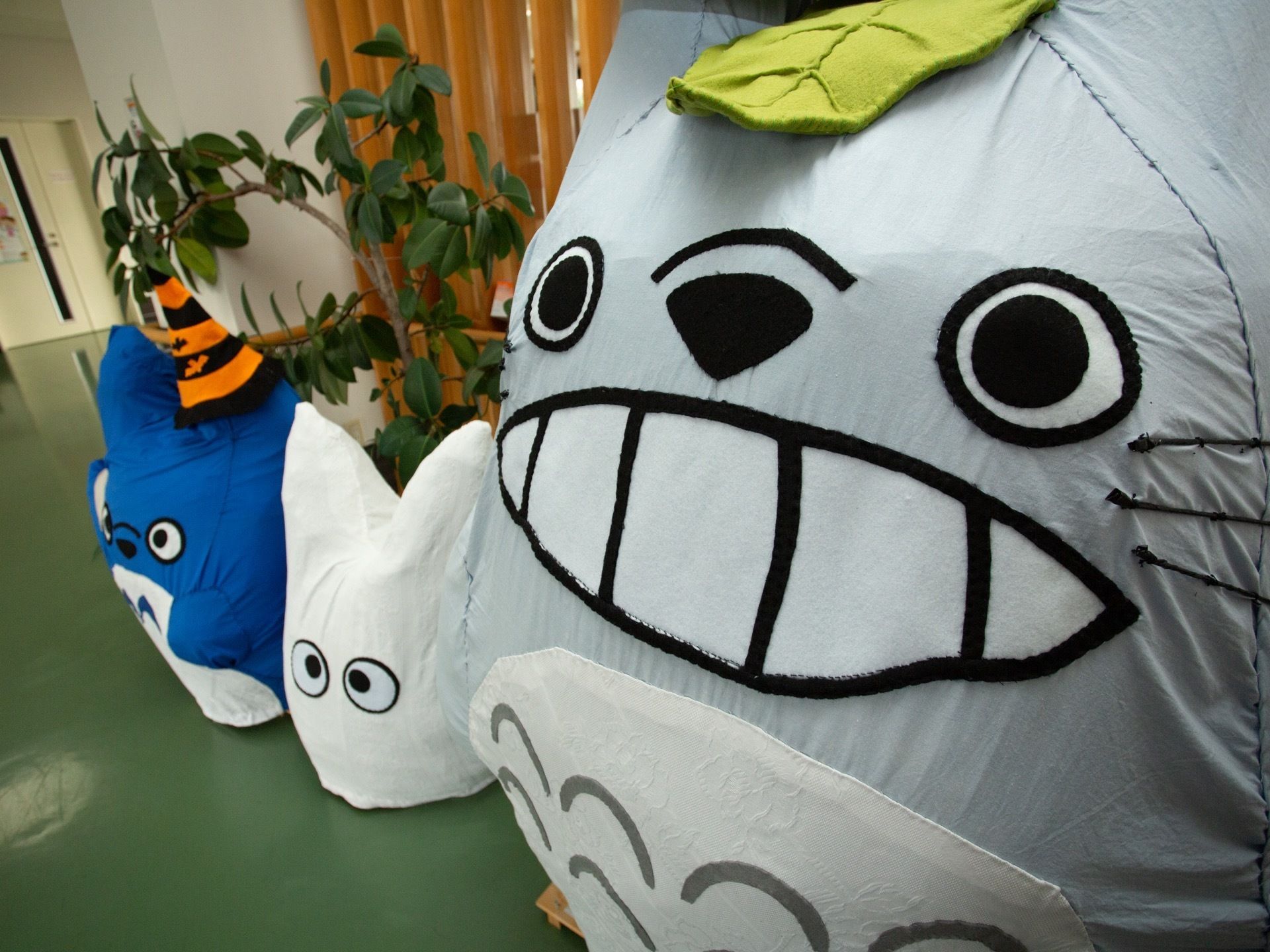 廊下に人気キャラクターの人形が３体並んでいる。全て手作りである。人形の奥に、観葉植物が置かれている。