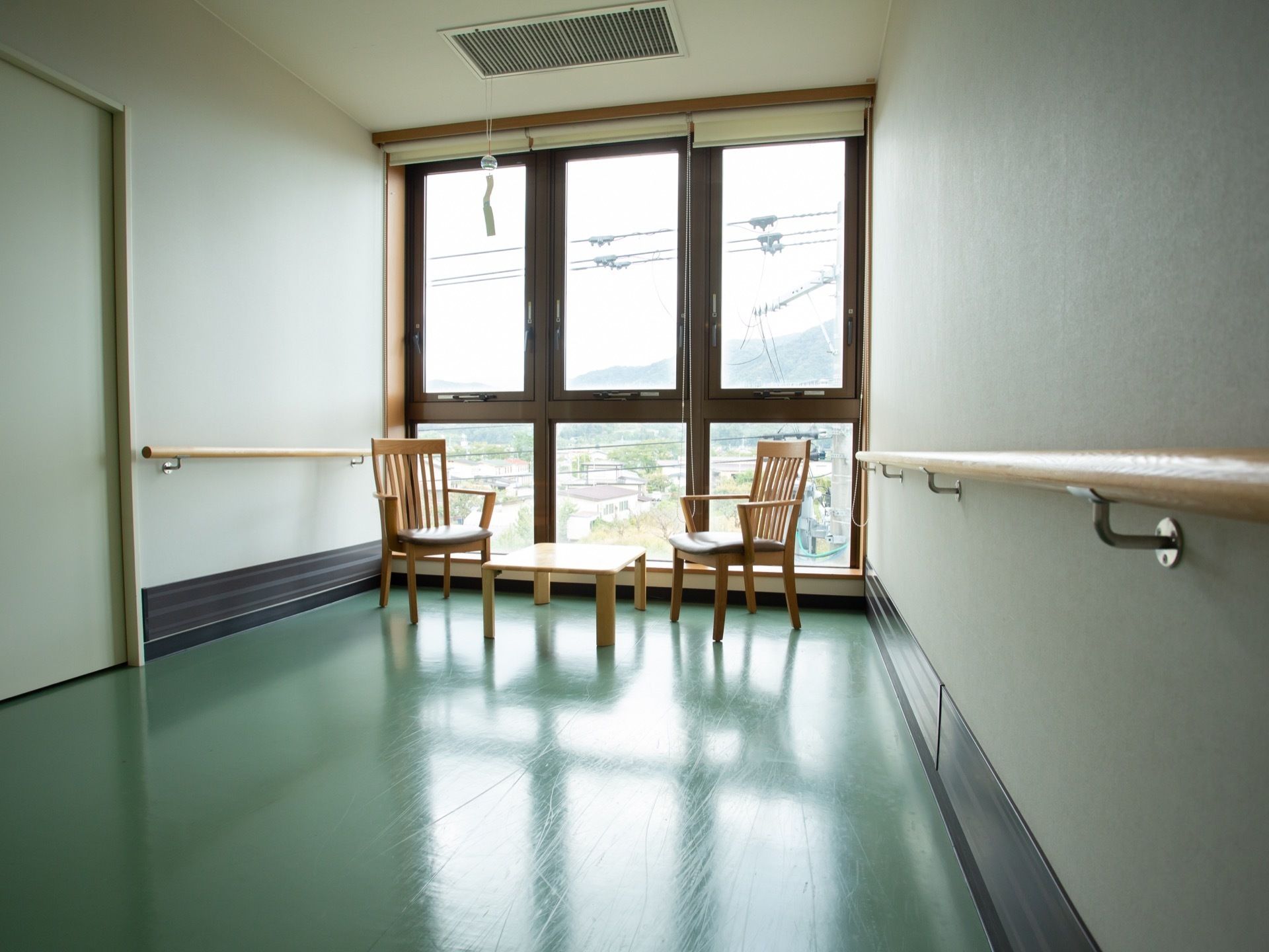 廊下の突き当たりの大きな窓際に、小さなテーブルを挟んで椅子が2脚置かれている。窓には日除けのロールスクリーンが備わっている。