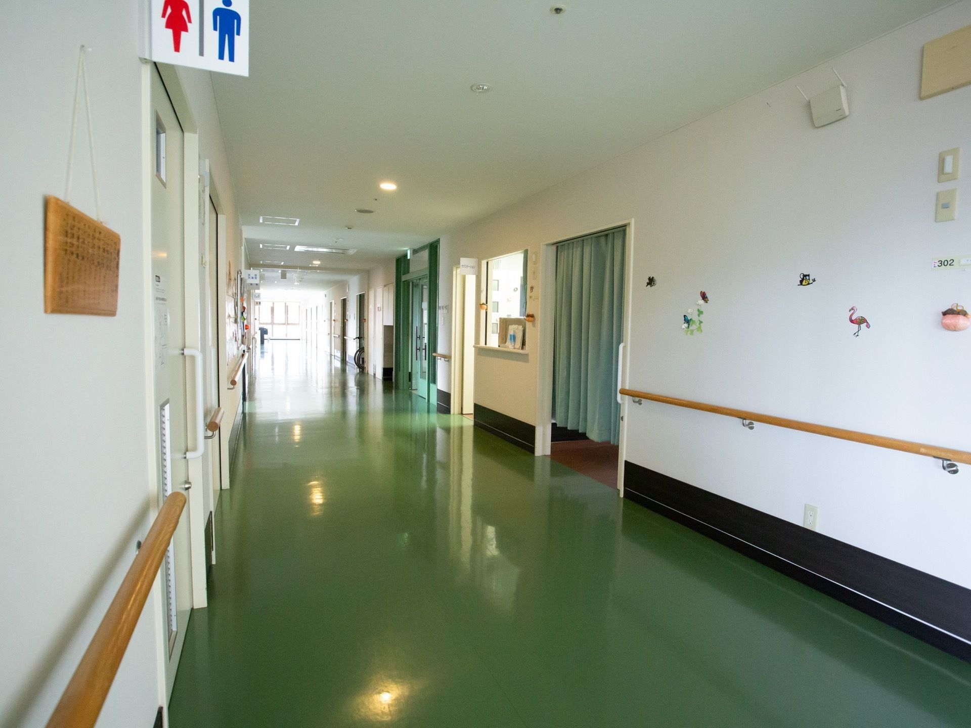 横幅の広い通路で、両脇の壁に手すりがある。共有トイレのドアはスライドドアで、スタッフルームの入り口はカーテンになっている。