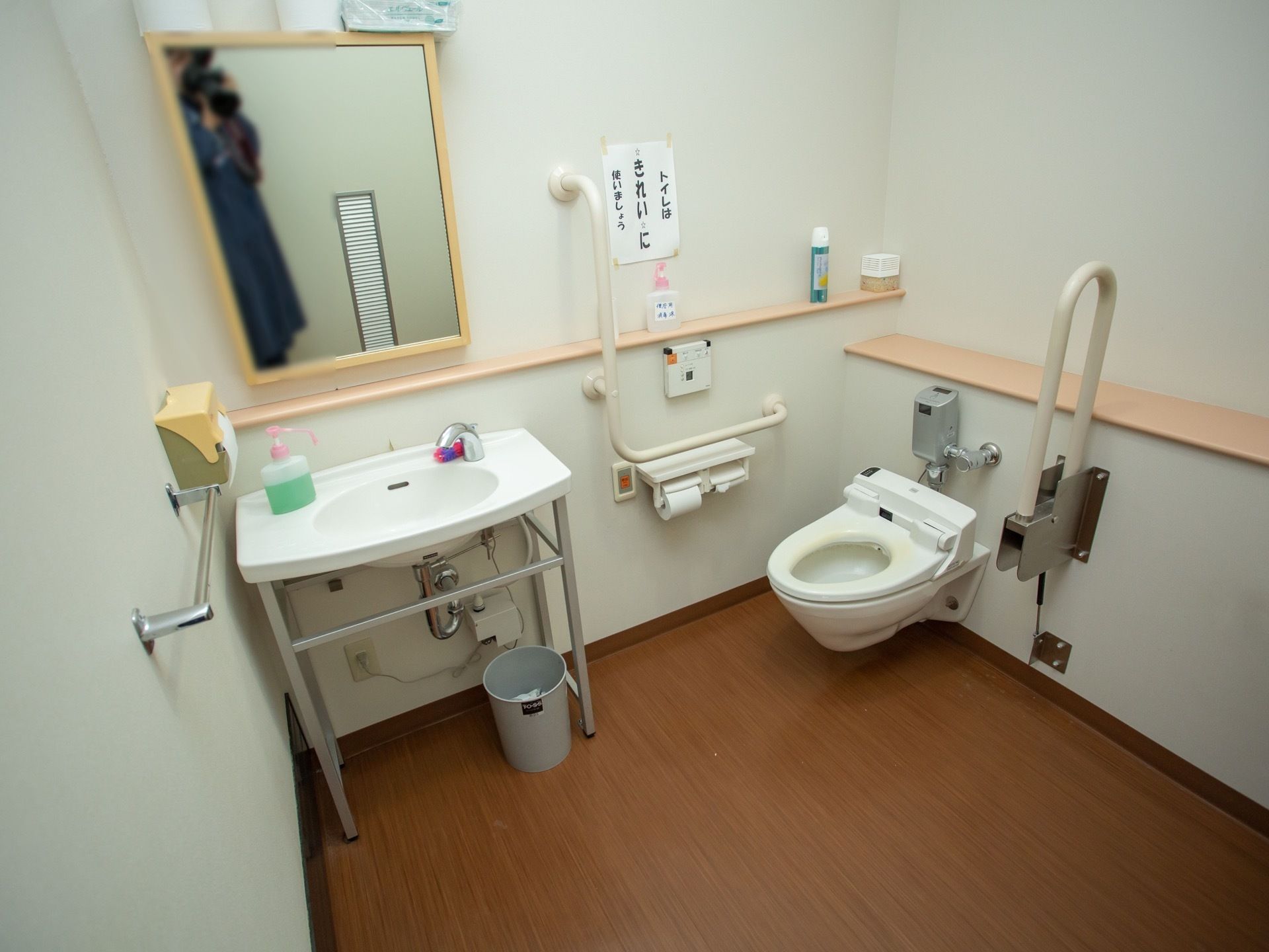 広い個室内に、洗面台や跳ね上げ式の手すりが備わっている。壁には手すりと自動洗浄便座のリモコン、ナースコールが取り付けられている。