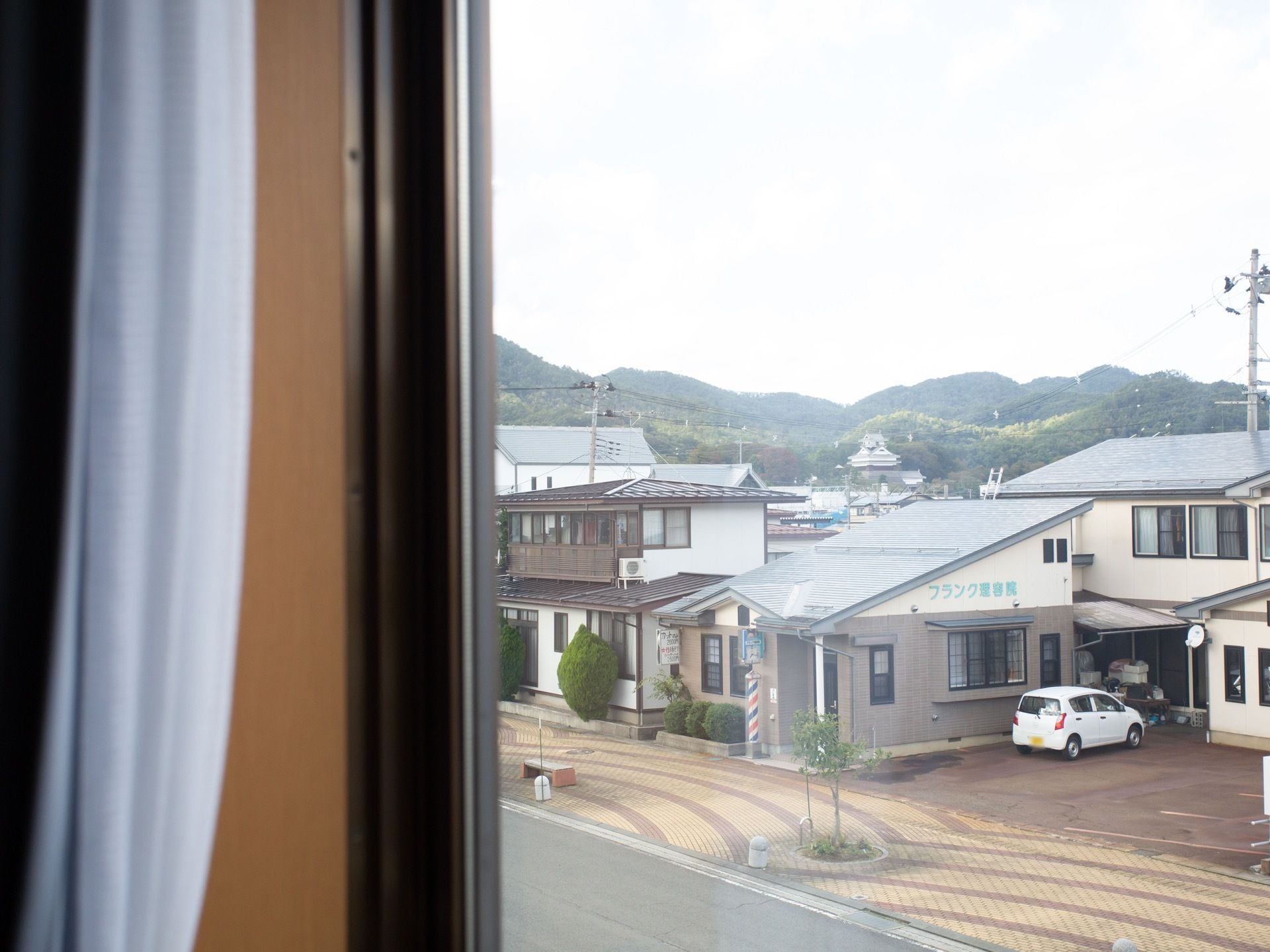 カーテンを開けて、周りの景色を見ているところである。民家や理容室、お城と共に、遠くに山々が見渡せる。