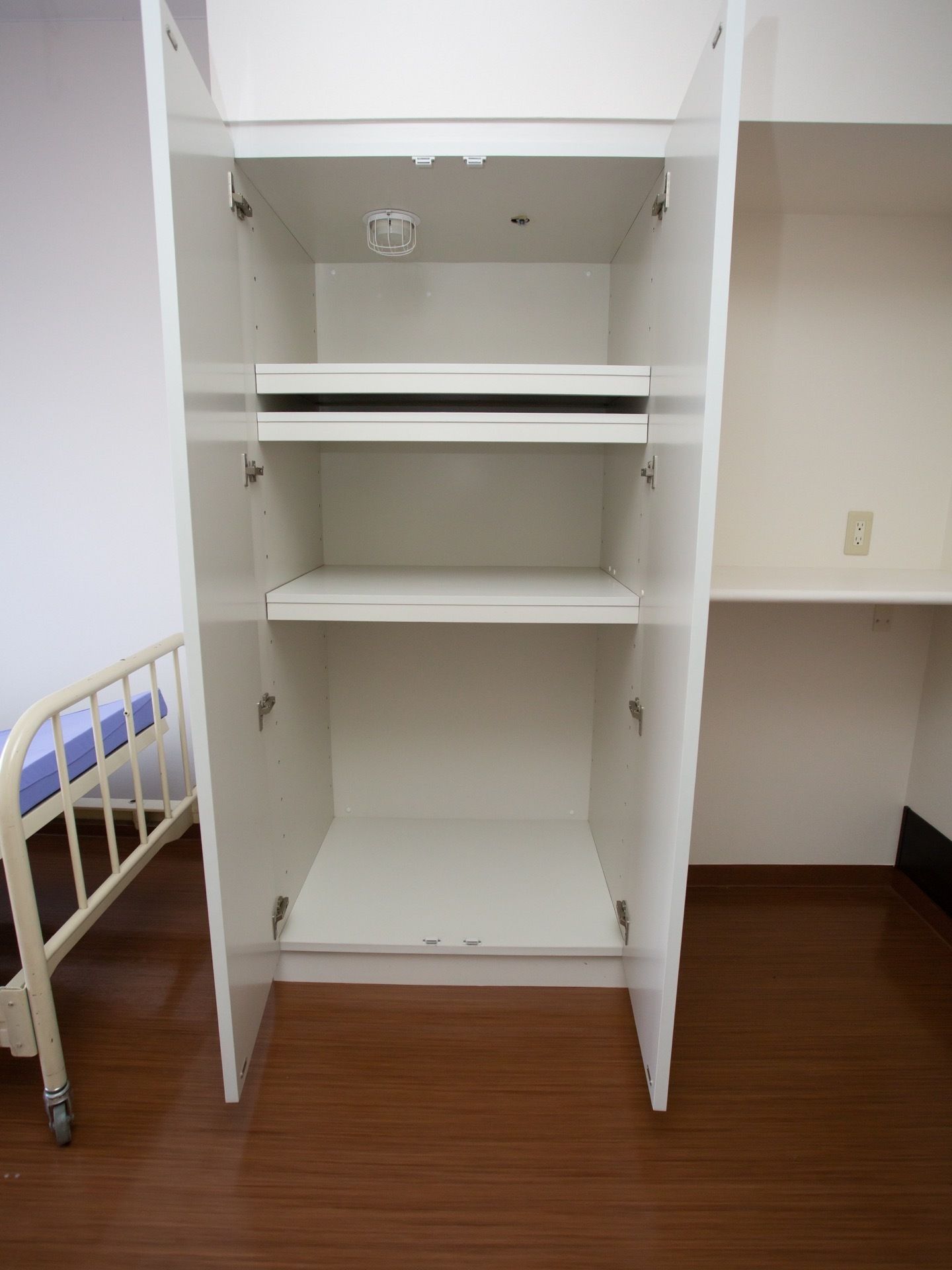 フローリングの室内で、左側にベッド、正面に収納棚が備わっている。棚にはたくさんの棚板が設置されている。