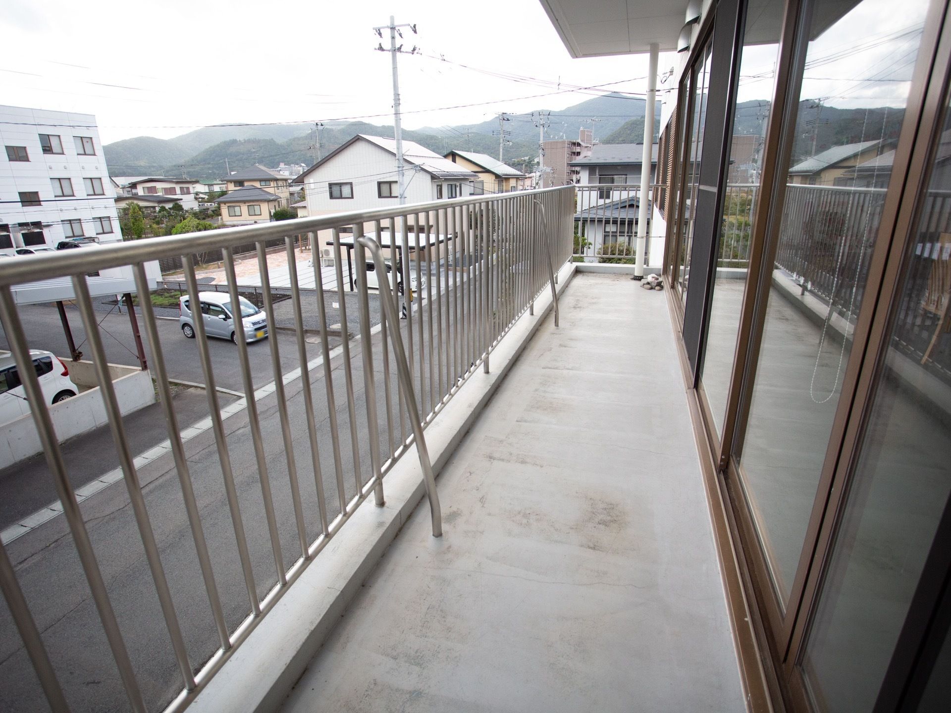 茶色の窓枠の大きな窓が並んでおり、外にベランダがある。ベランダはコンクリート貼りで、銀色の柵が備わっている。