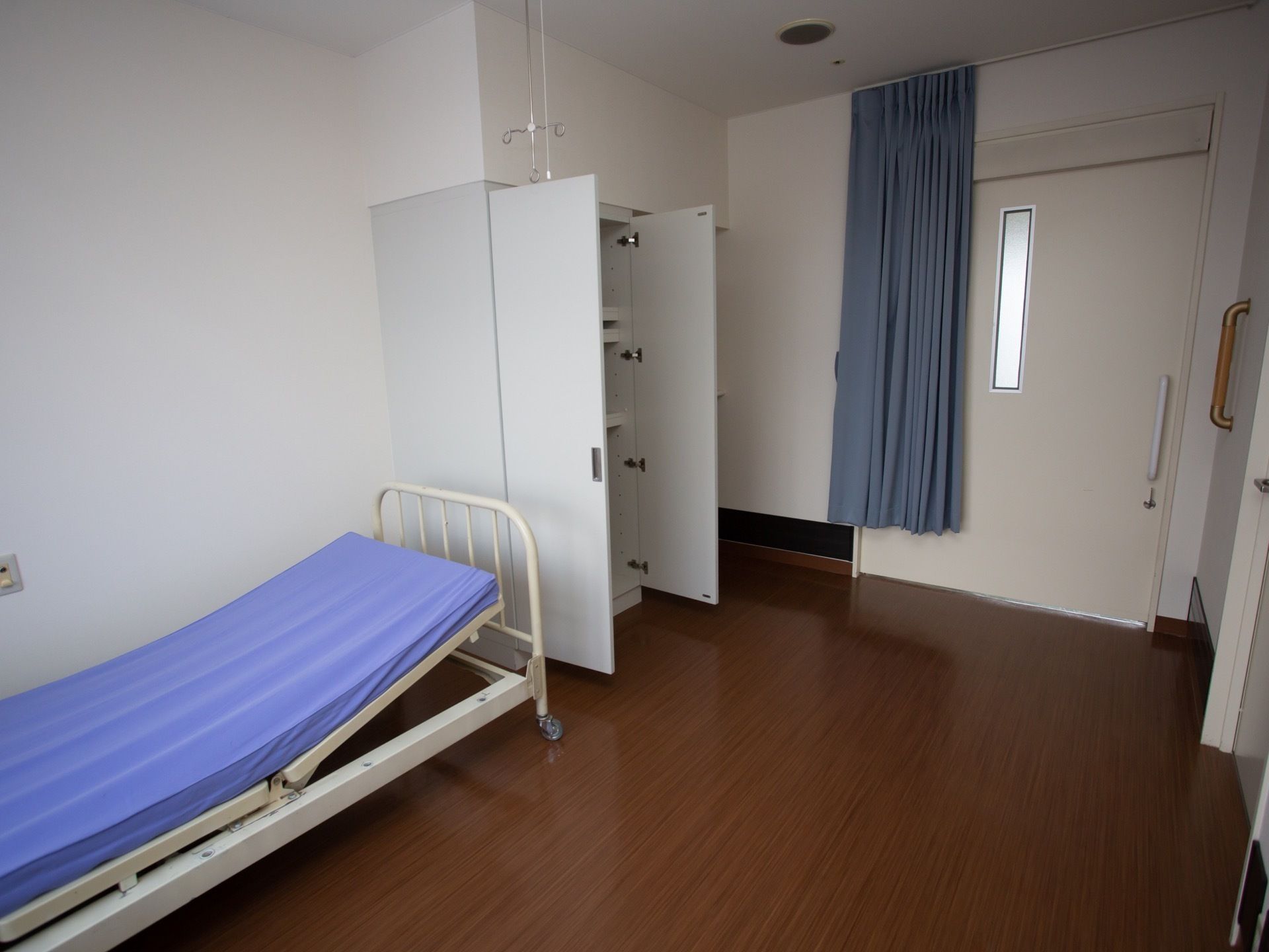 大きなスライドドアの入り口の部屋で、右側にトイレのドアがある。左の壁際に、収納棚と介護ベッドが備わっている。