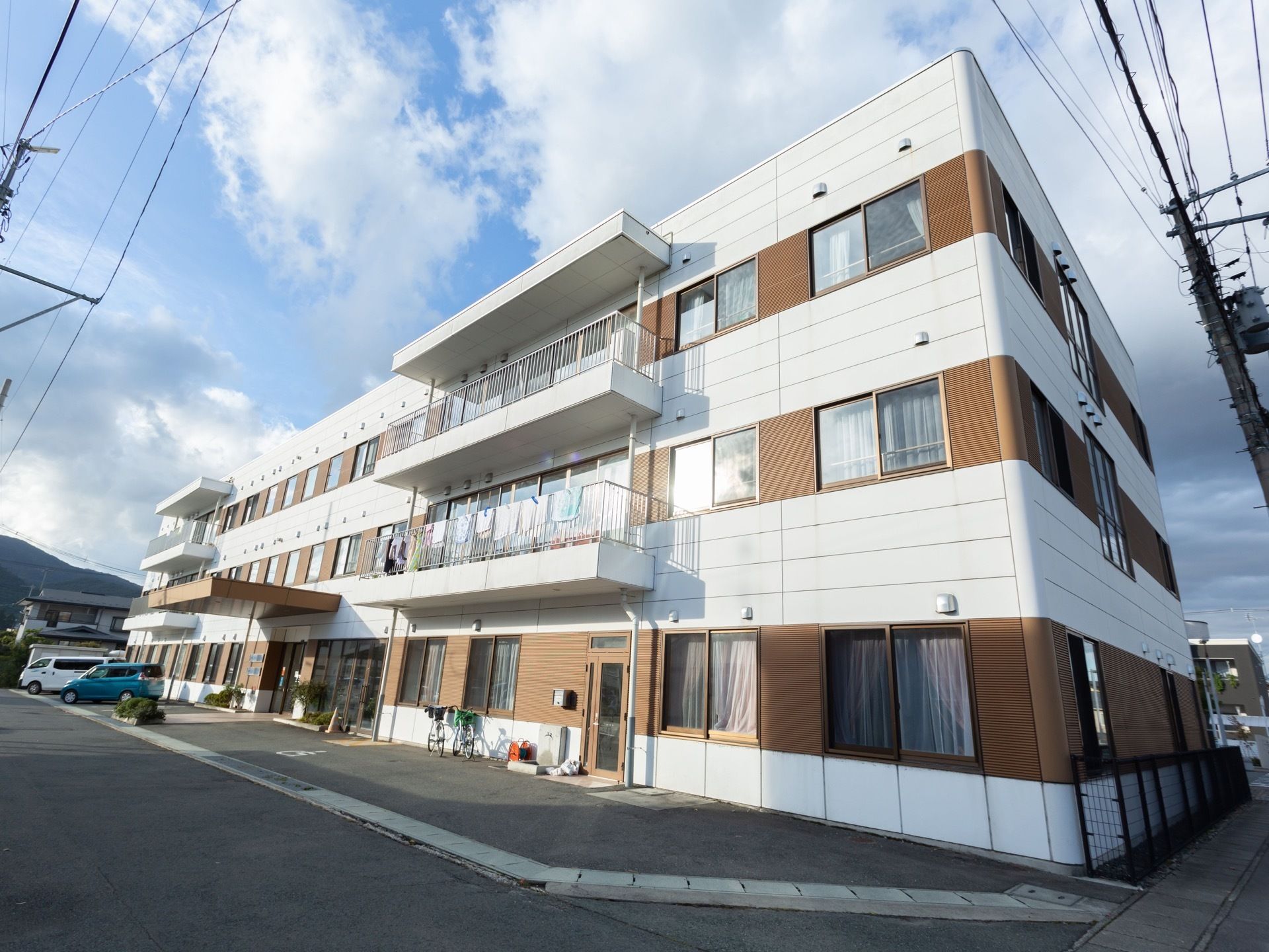 ３階建ての建物で、白色に茶色のアクセントの入ったツートンカラーの外壁である。建物前に駐車スペースが設けられている。