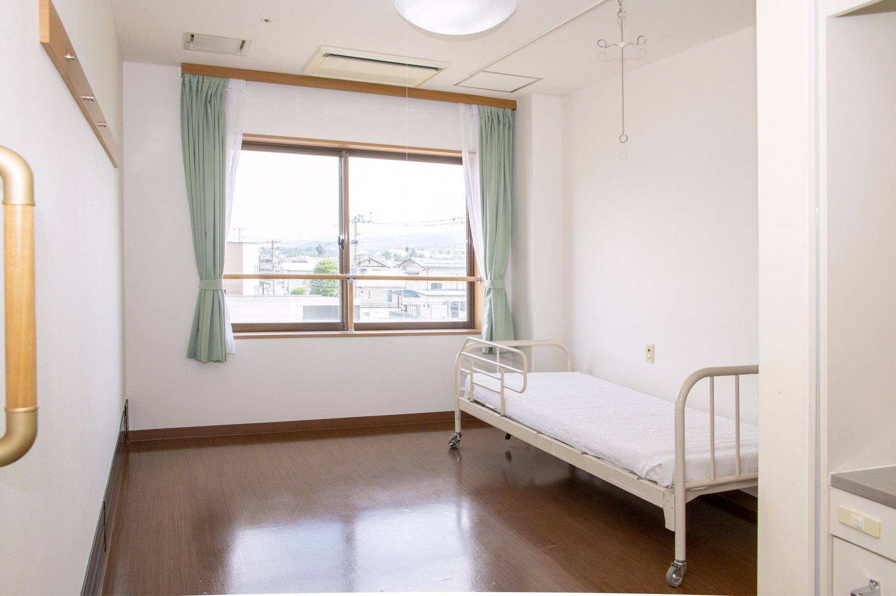 リクライニング機能の付いた電動介護ベッドと収納棚が置かれている。ベッドにはブルーのカバーのついたマットレスが備わっている。