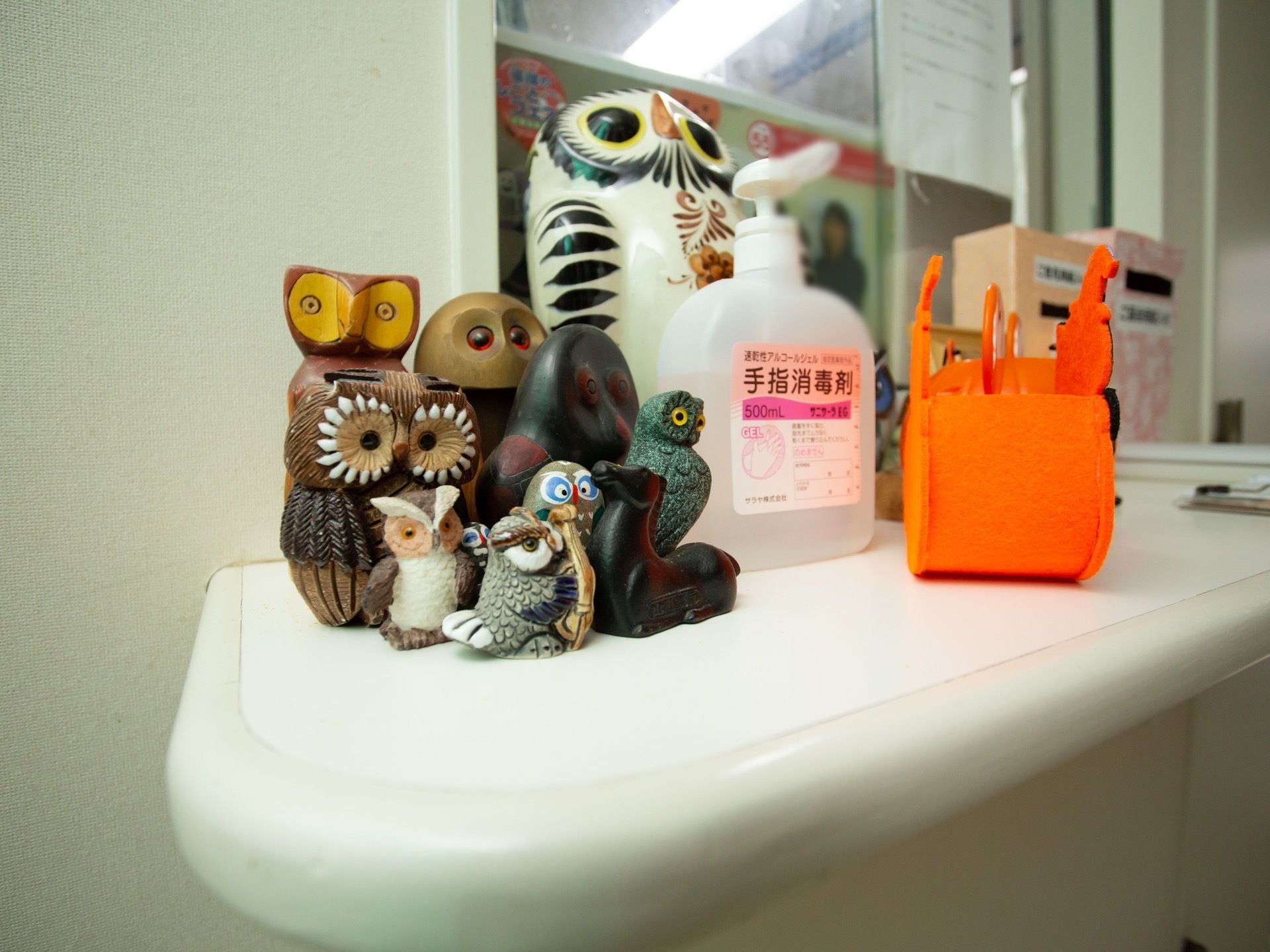 受付の小窓の前にあるカウンターには、色や形、大きさの異なるフクロウの置物が置かれている。アルコール消毒液も備わっている。