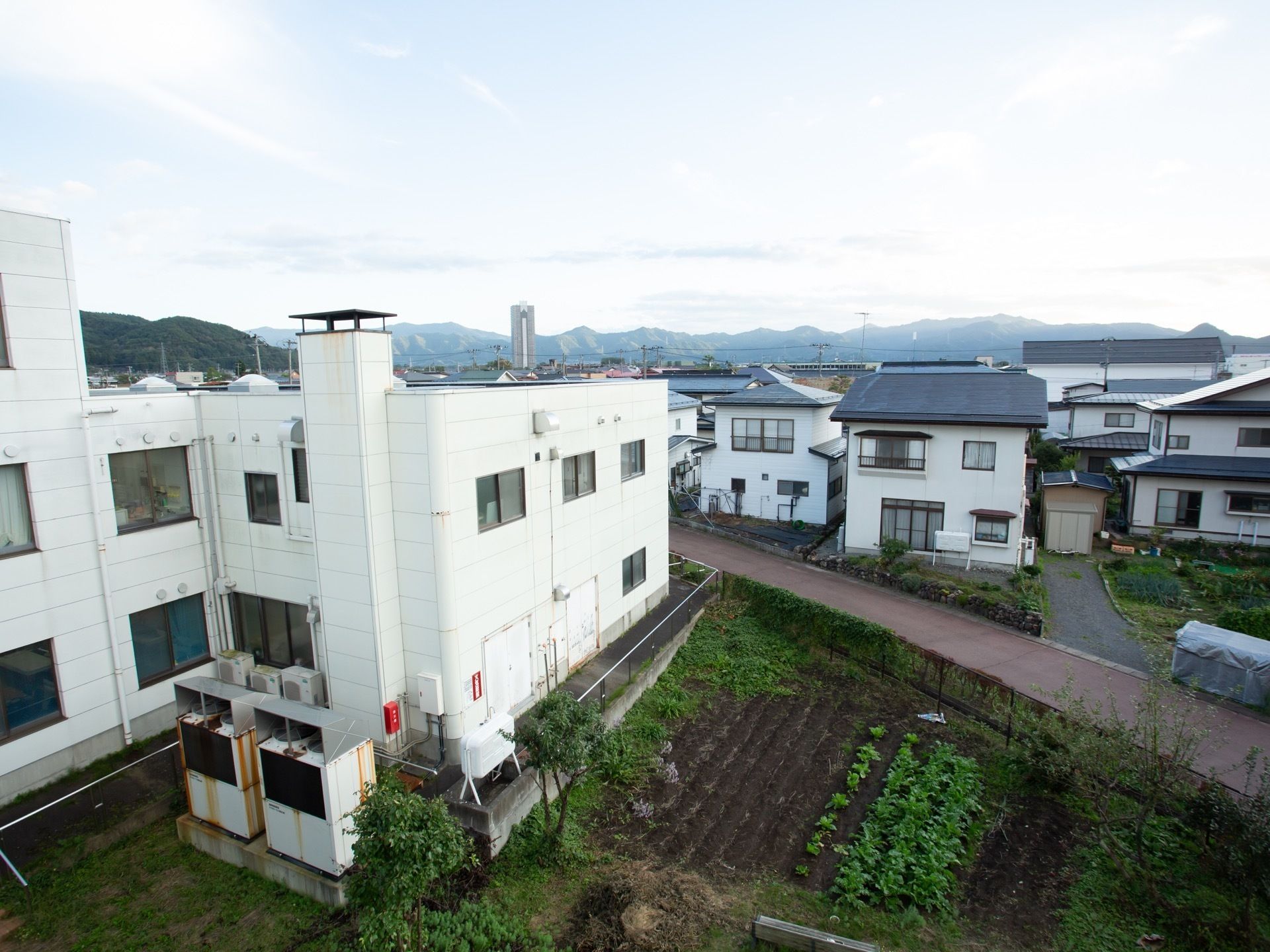 施設の上層階から眺めた、施設の周辺の景色である。近隣には民家や田畑があり、遠方には山が連なっている。