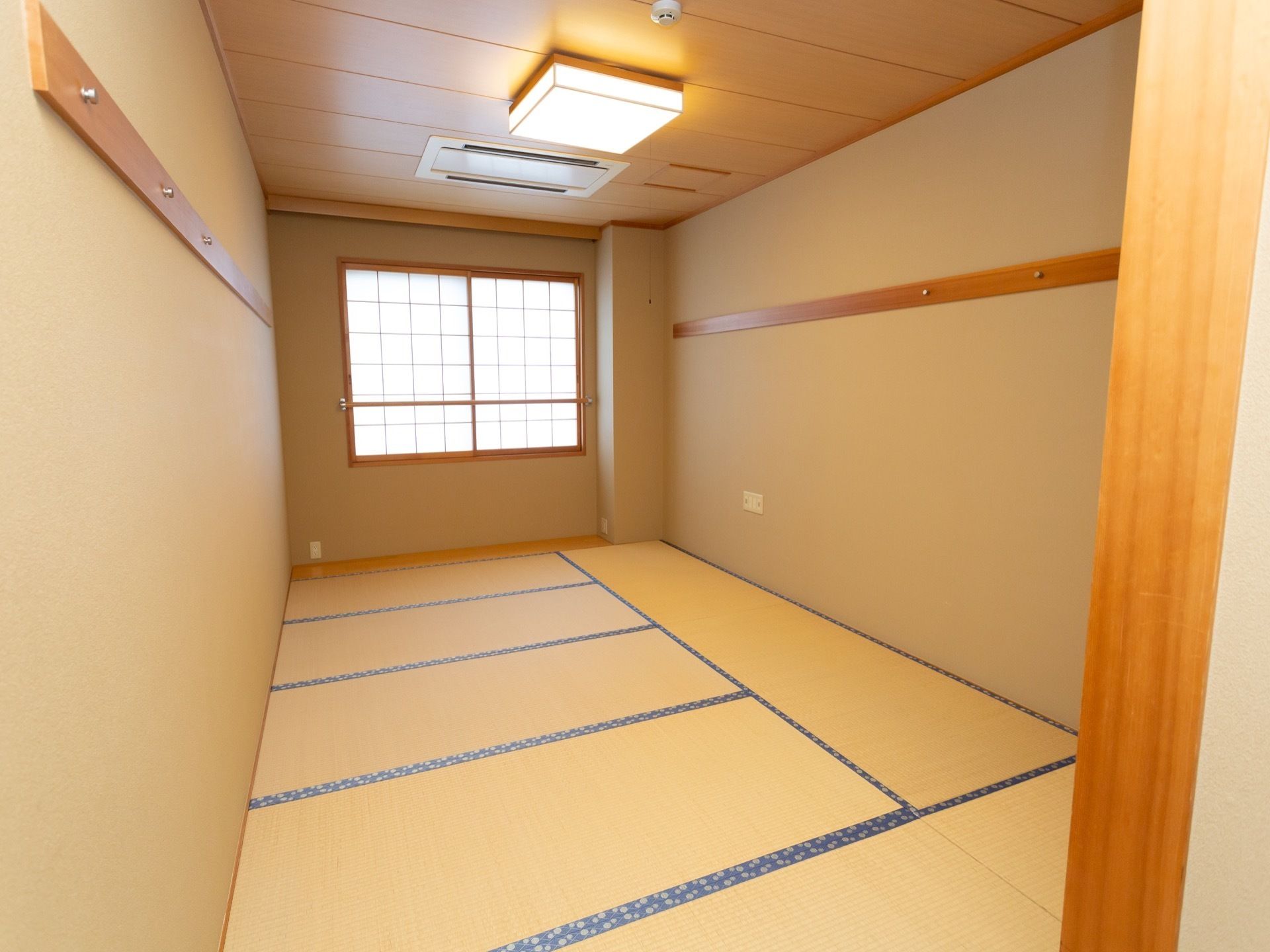 約８畳の和室の居室である。天井にはシーリングライトが備わり、壁にはハンガーを掛けられるフックが取り付けられている。