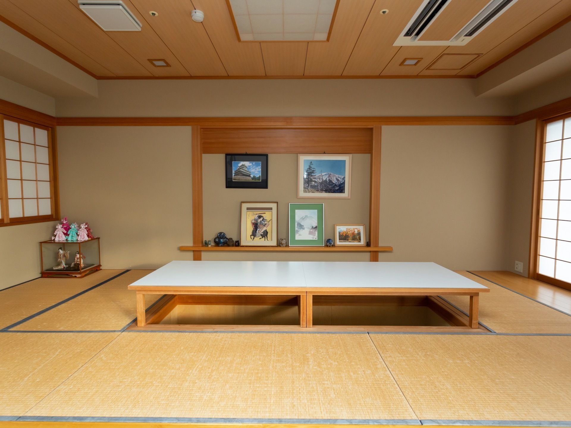 和室の共有スペースである。部屋の中央には大きなテーブルが置かれ、足元は掘りごたつになっている。壁には額に入った写真などが掛けられている。