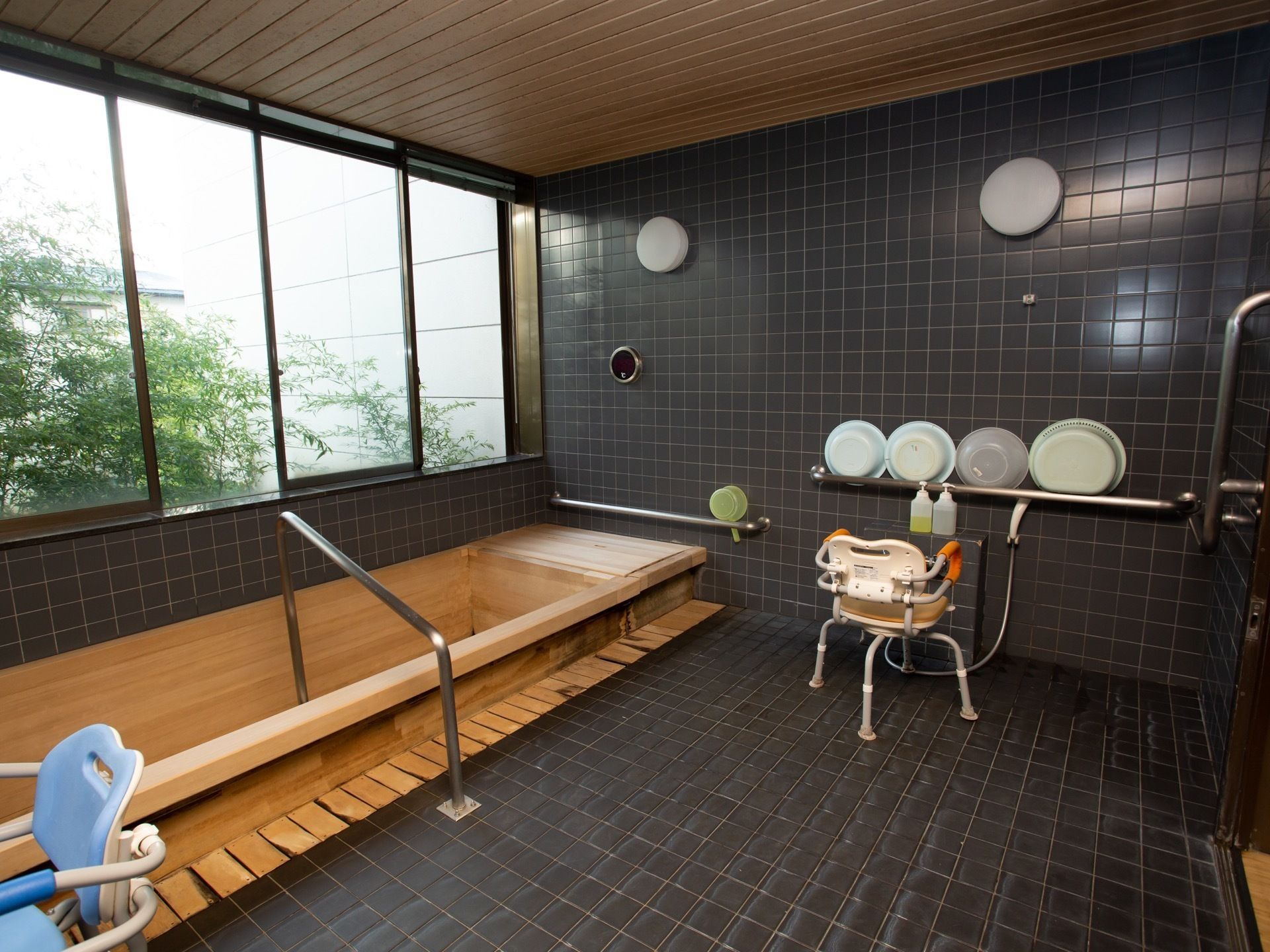 黒色のタイル張りの大浴場である。木製の大きな浴槽が備わり、大きな窓からは、屋外の緑の葉が茂る木々を見ることができる。