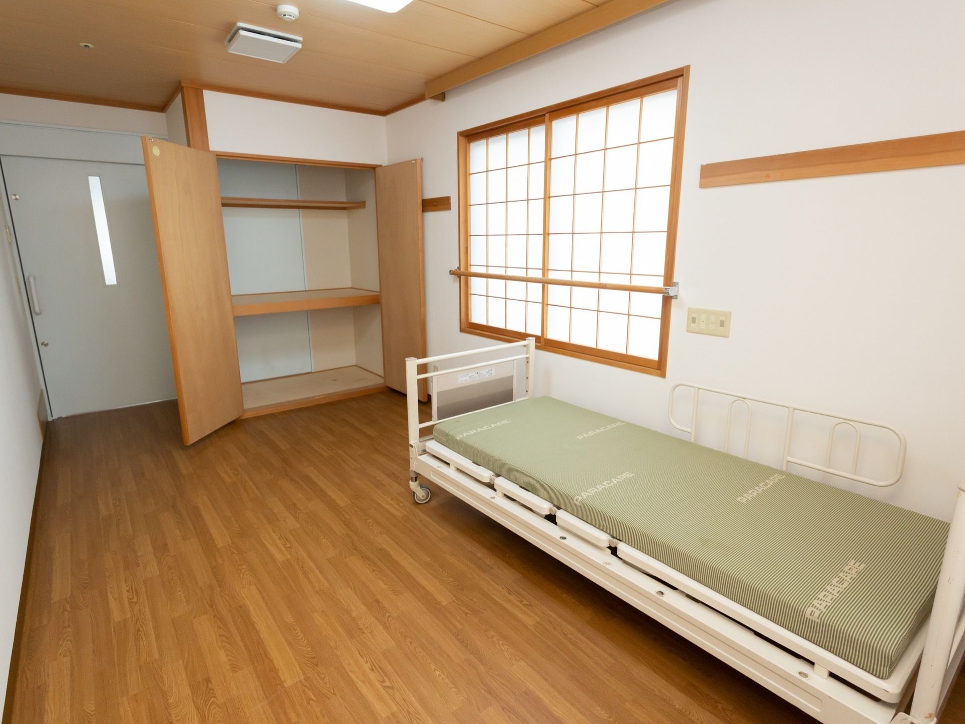 フローリングの居室にはベッドが１台備わっている。観音開きのクローゼットの中には棚が設けられ、空間が３段に分けられている。