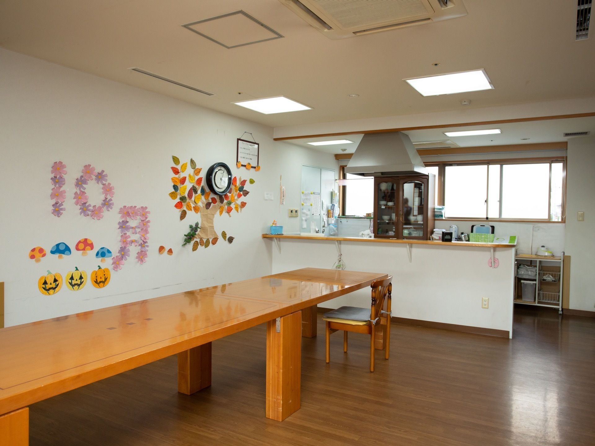 対面式キッチンが備わる共有スペース。長方形のテーブルがある。白色の壁には折り紙や画用紙で製作した作品が飾られている。