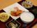 トレーの上に、ご飯、味噌汁、おかずが並んでいる。それぞれ陶器の器に盛られている。箸とスプーンが置かれている。