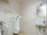 広々としたトイレスペースである。男性専用の便器の前方の壁際に、シンプルな白い洗面台を備えている。傍に水を止めることを促す張り紙を貼っている。