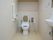 ゆったりとしたトイレスペースの便座の横の壁に、エル型の手すりを設置している。後部の上の方には予備のトイレットペーパーなどが置ける棚がある。