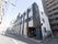 地上３階建ての施設全体を、斜め方向から写したものである。建物の左側には道路があり、その上方には青空が広がっている。