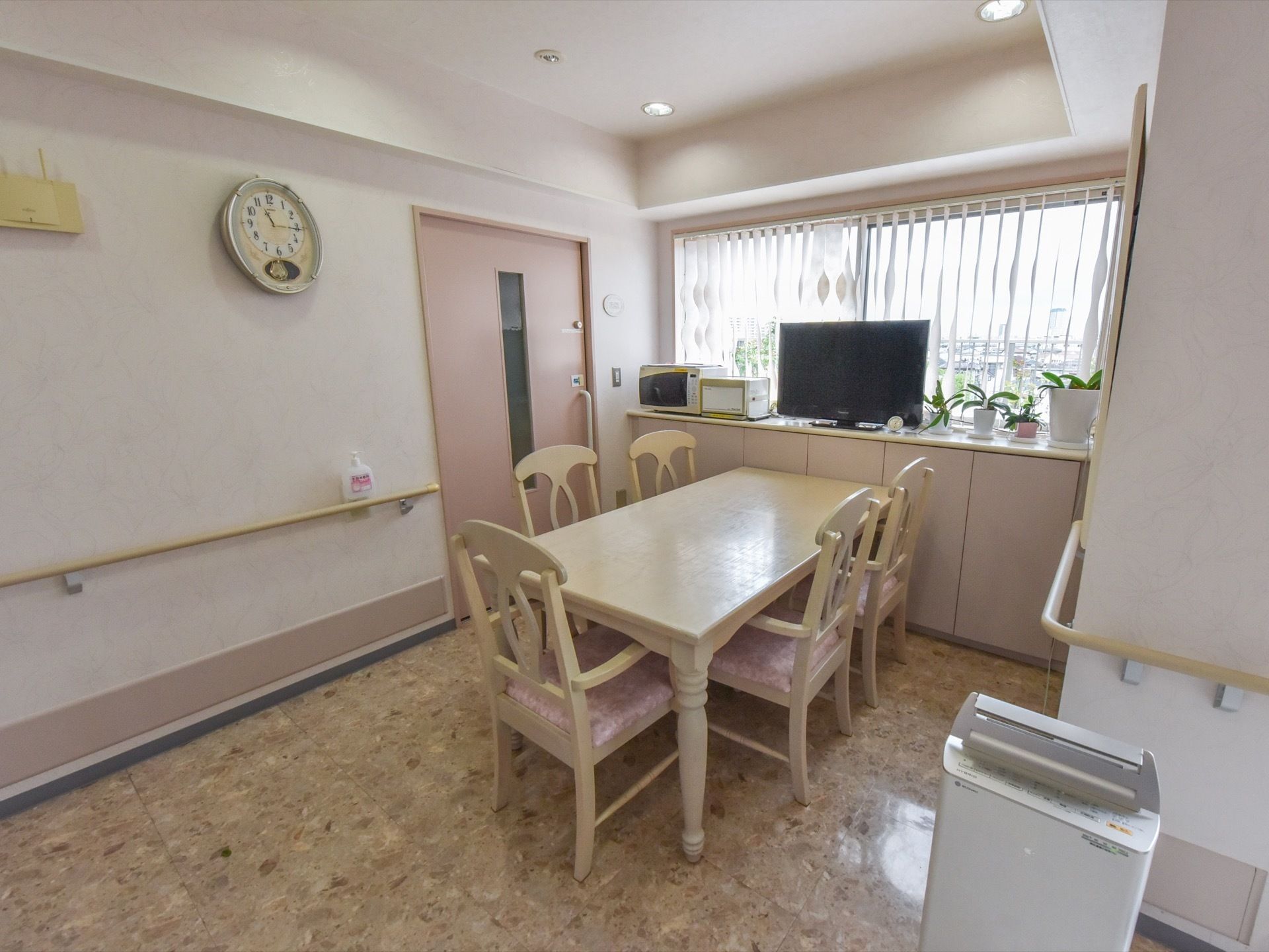 入居者様が共有している部屋には、テレビ・電子レンジなどの家電とテーブルセットが置いてある。壁には手すりを設置している。