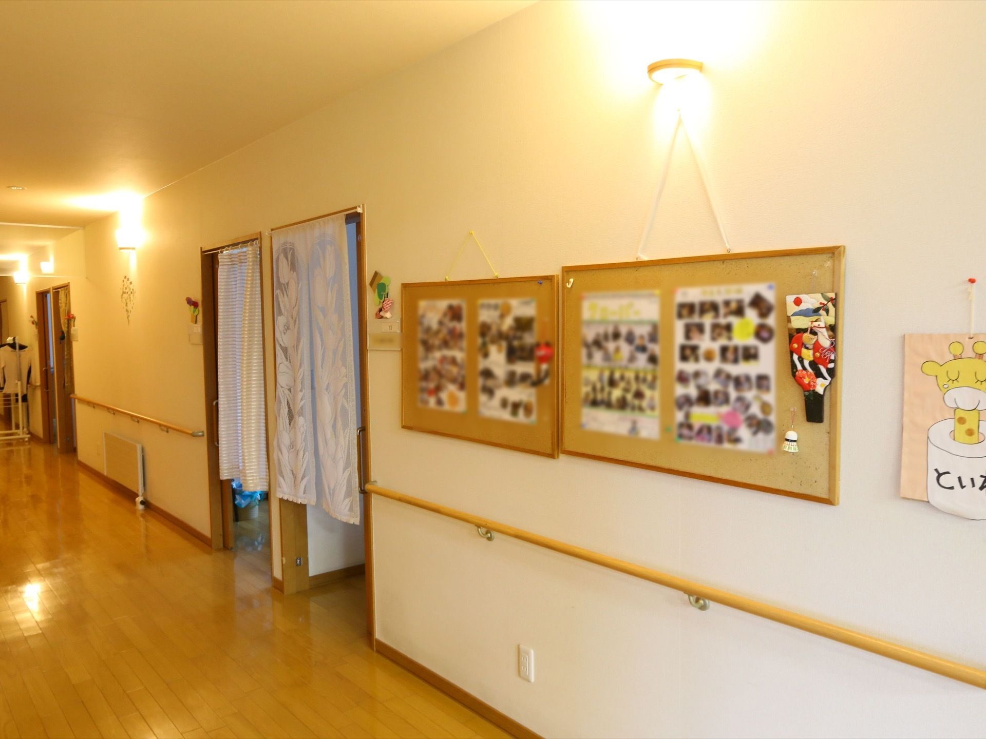 施設の廊下の白い壁に、掲示ボードが2つ並べて掛けられている。さまざまな記念写真がレイアウトされている。