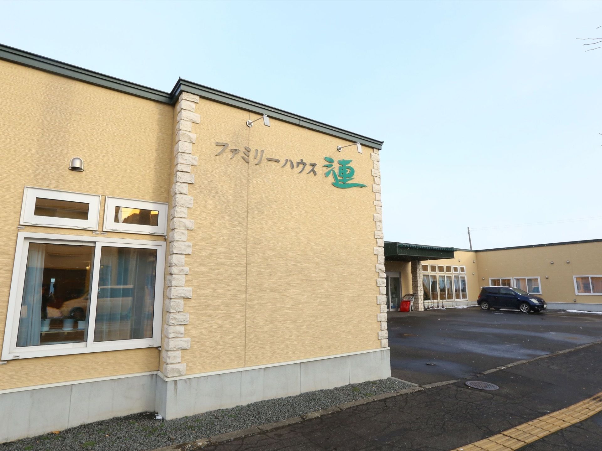 駐車場を完備した1階建ての施設は、イエロー系の外壁に施設名称を表記している。訪問介護やデイサービスを併設している。