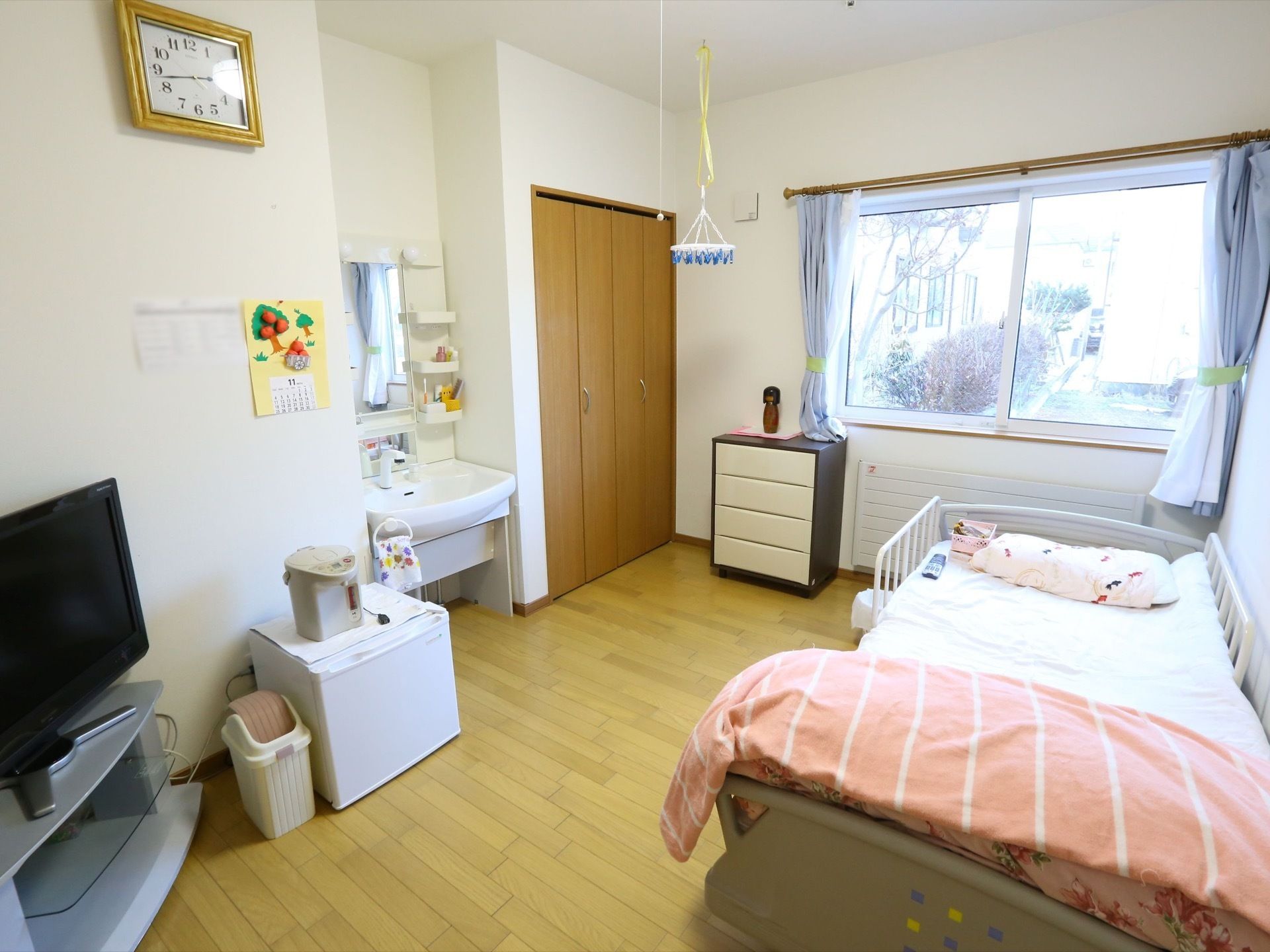 窓や介護用ベッドが設置された居室である。テレビやハンガーなど入居者様のお好みにレイアウトされている。