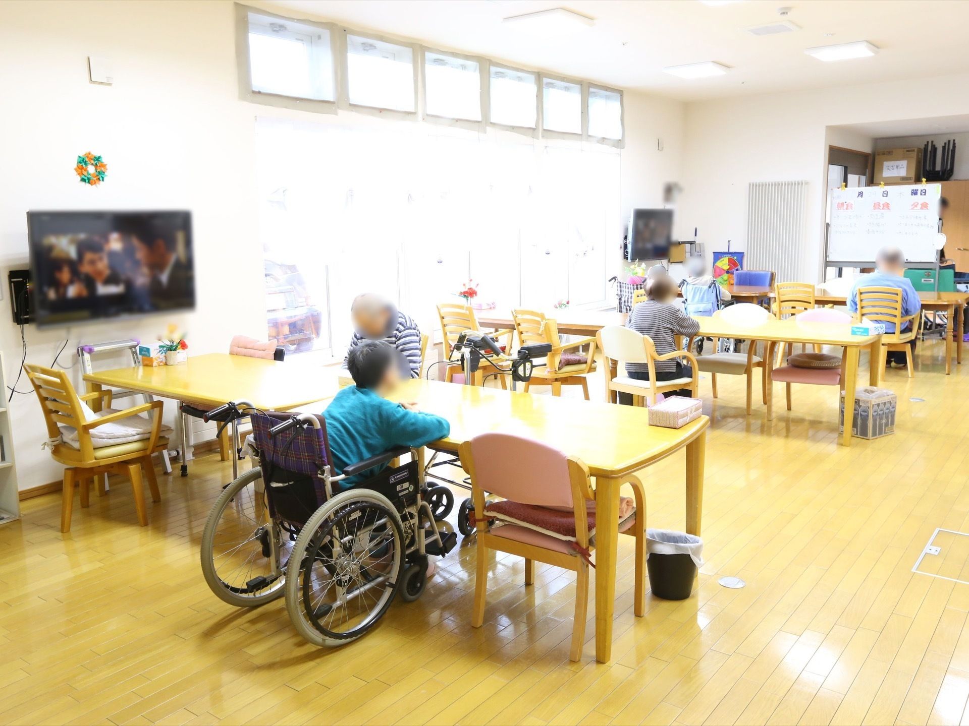 共有スペースでは、ゆったりとした配置でテーブルセットが設置され、席に着く数名の入居者様の姿が見える。