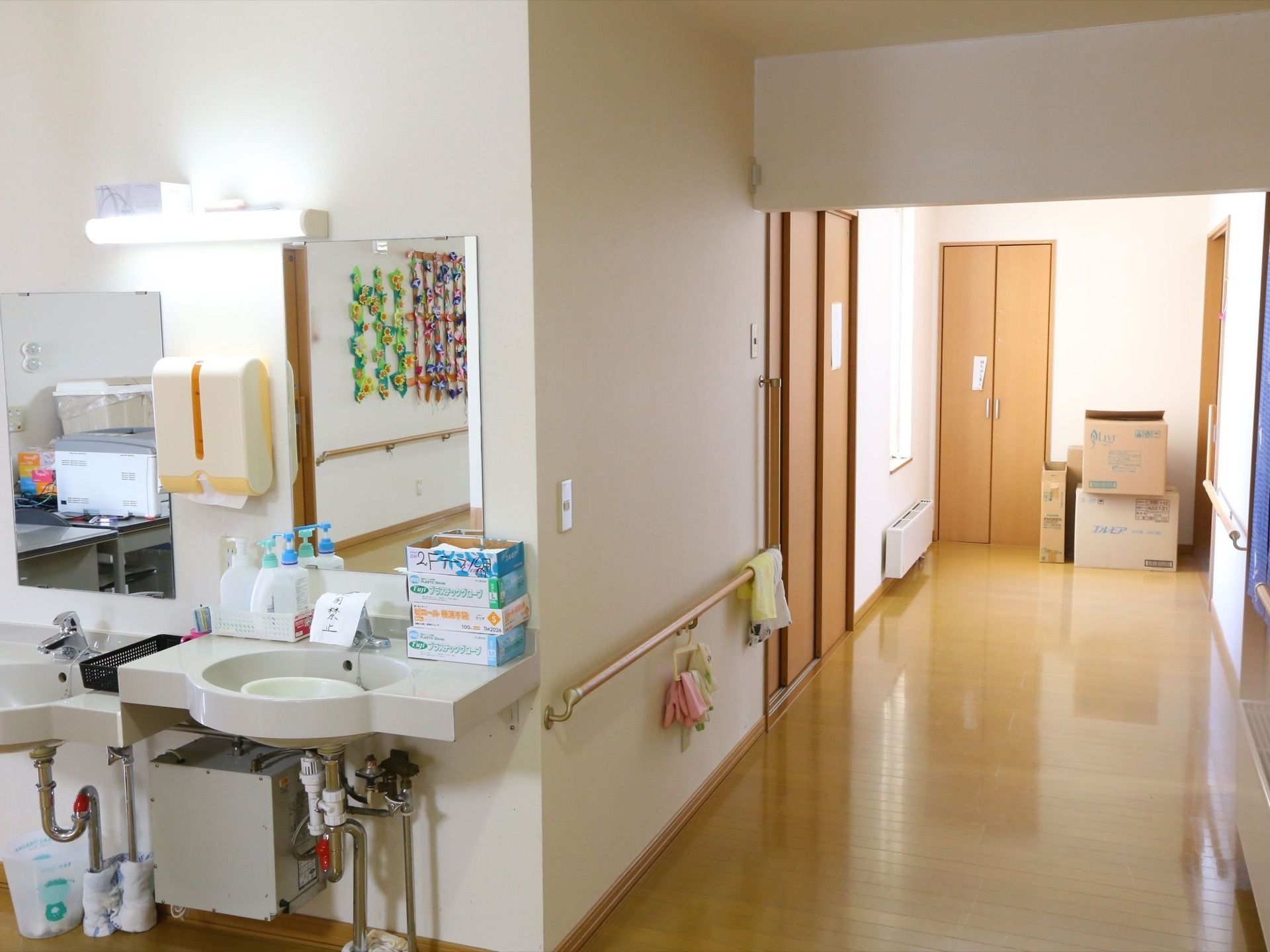 茶色の木製のドアが並んでいる広い廊下がある。角には二台の洗面台と鏡があり、衛生用品とペーパータオルが置かれている。