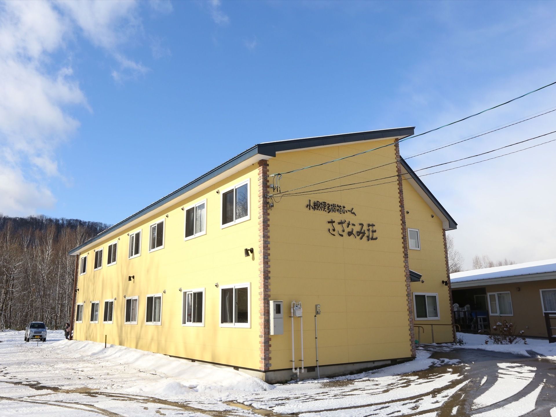 黄色い壁の二階建てで斜めの屋根がついている、大きな建物がある。近くには山があり、周囲には高い建物がなく見晴らしがよい。