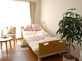 居室にはベッドが備え付けられている。１人用のテーブルセットが置かれ、観葉植物の鉢植えが飾られている。