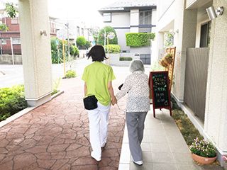 入居者様の手を優しく引いて、散歩に出かけるスタッフ