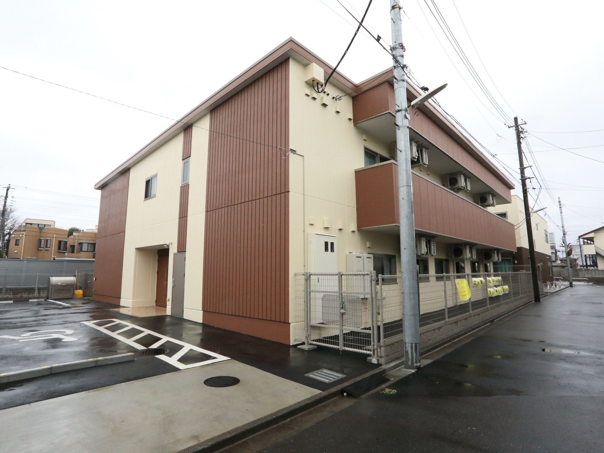 施設はベージュとこげ茶の２色の壁で、２階建てである。敷地内に駐車場がある。道路に面した窓がある部分には、フェンスが設置されている。