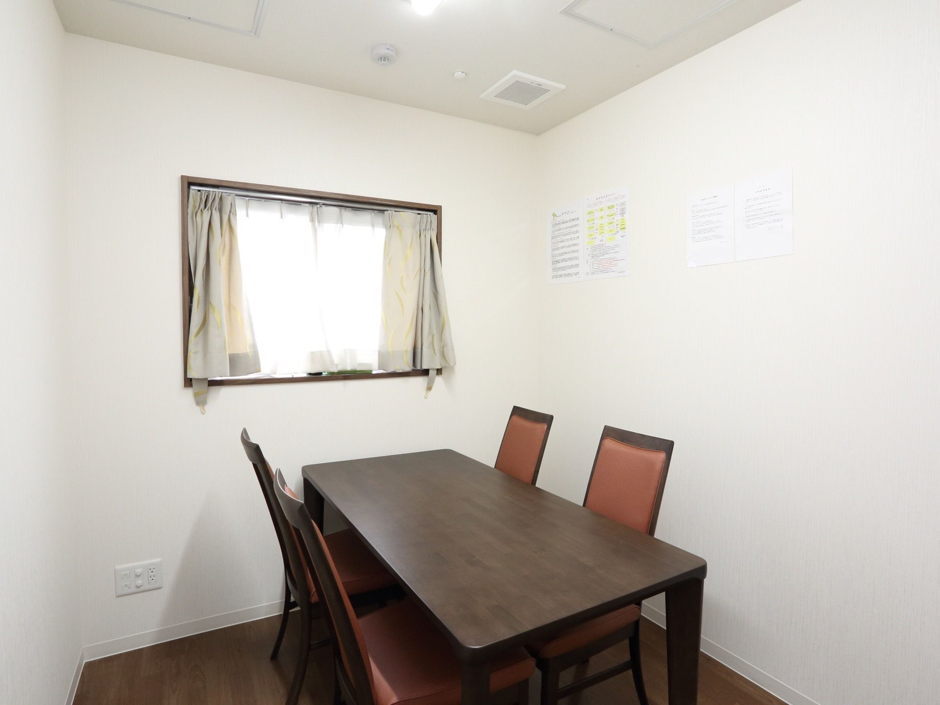 部屋には窓があり、カーテンが二重にかかっている。テーブルと４脚の椅子が設置してある。床はフローリングになっている。