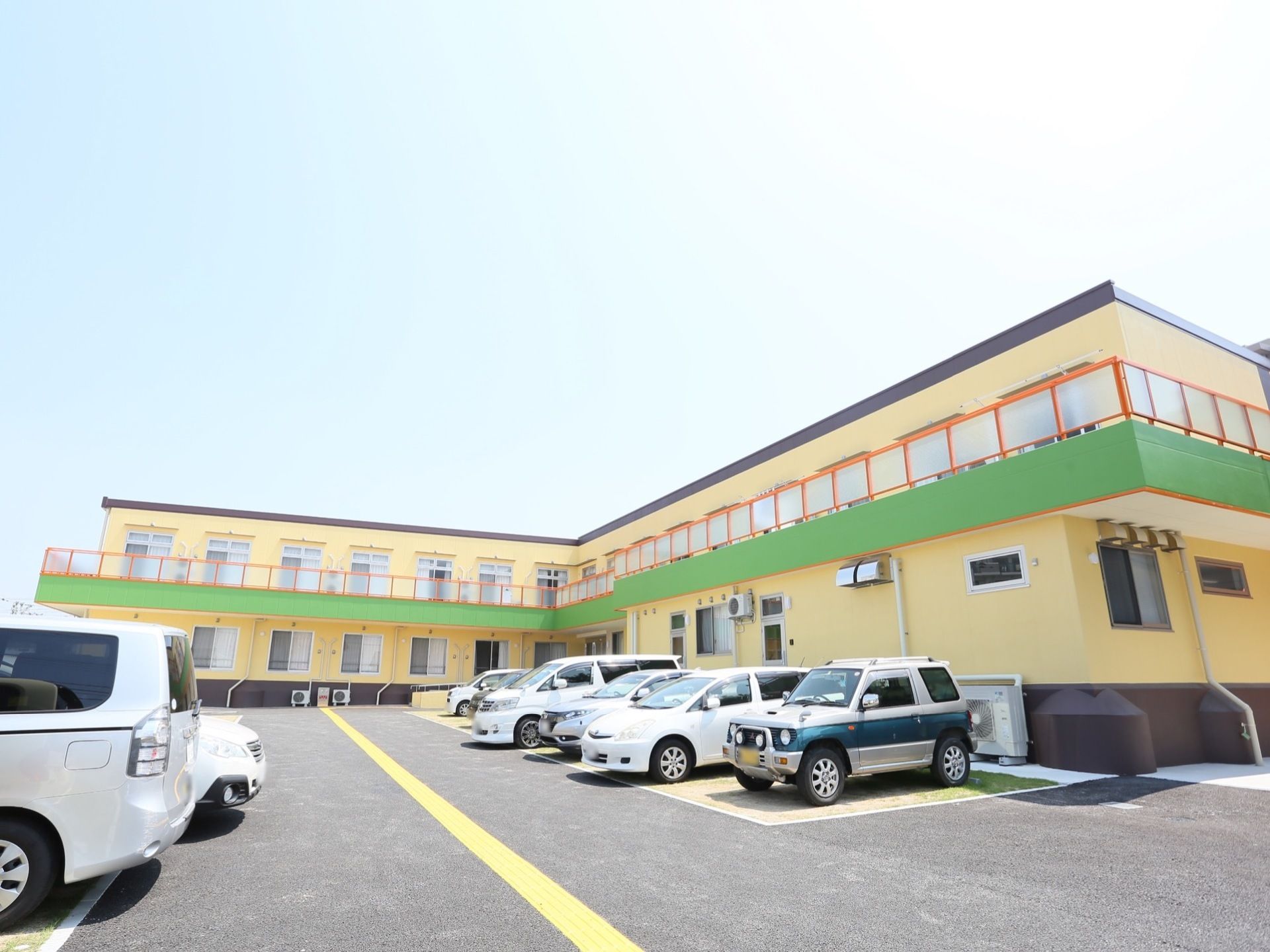 ２階建ての施設は、ライトイエロー、黄緑、オレンジの３色が組み合わされたカラフルなデザインである。左横には、駐車場がある。