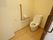 隅々まで清掃された清潔感あふれる居室内のトイレである。L字型の大きな手すりや、オレンジ色のコールボタンが壁についている。
