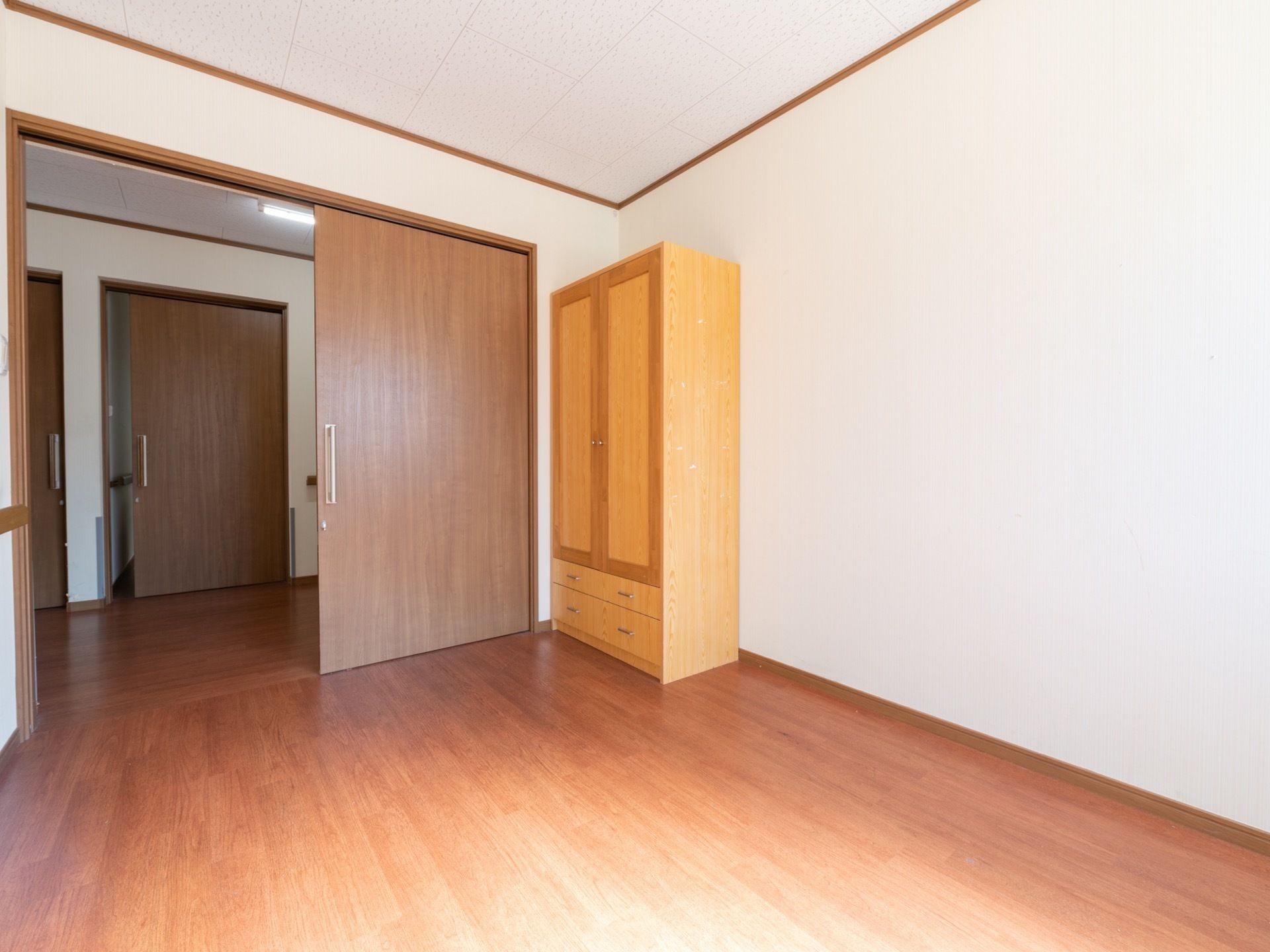 フローリングの部屋の角に、置き型の木製クローゼットがある。上は観音開きで、下に２段引き出しがついている。