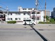 ２階建ての白いアパートタイプの建物である。入口の部分には屋根がついている。手前の道路には白いバンが一台停まっている。