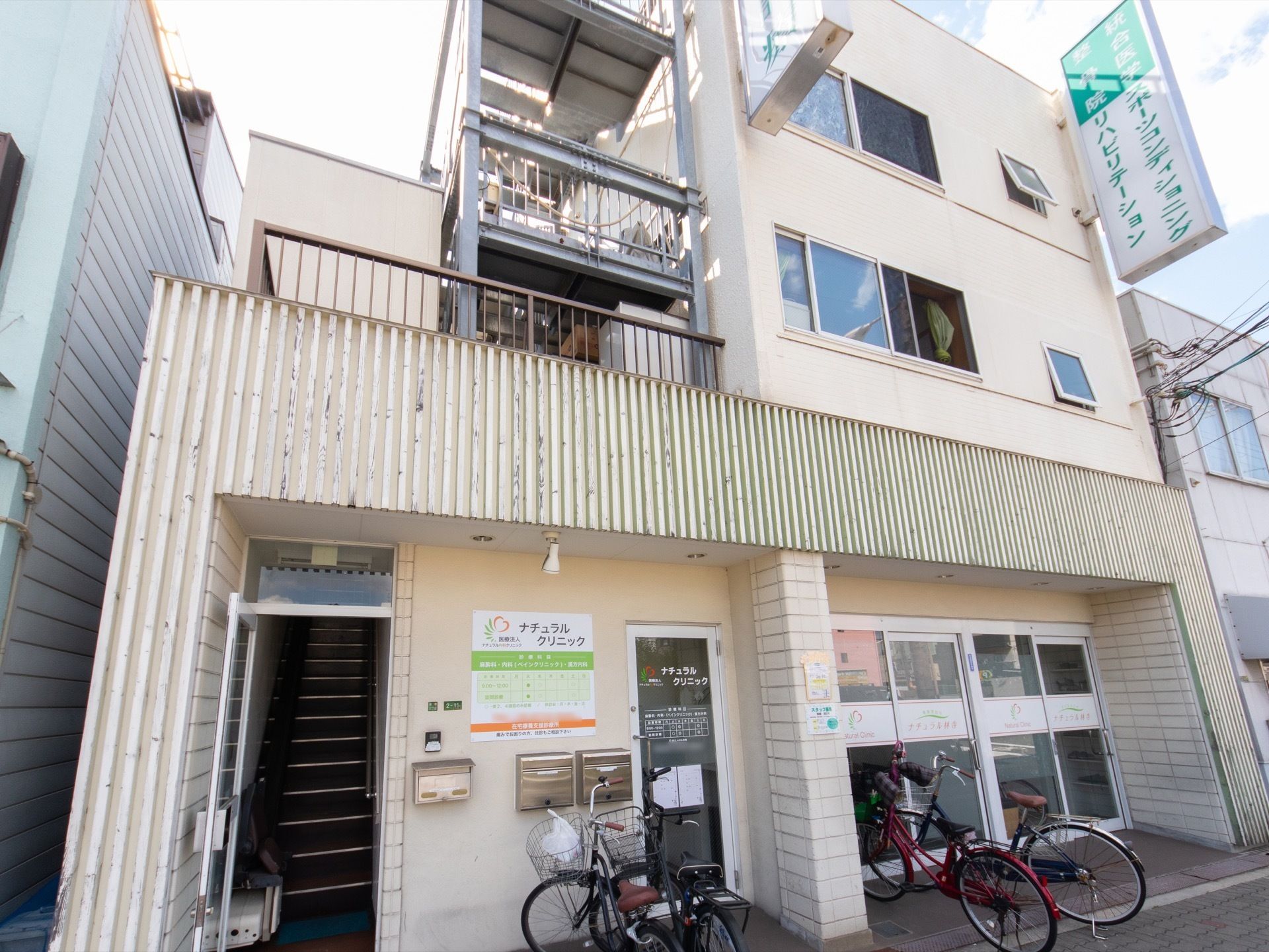 施設は道路沿いに立地しており、クリニックと隣接している。バリアフリー仕様の入り口の前に自転車が数台止まっている。