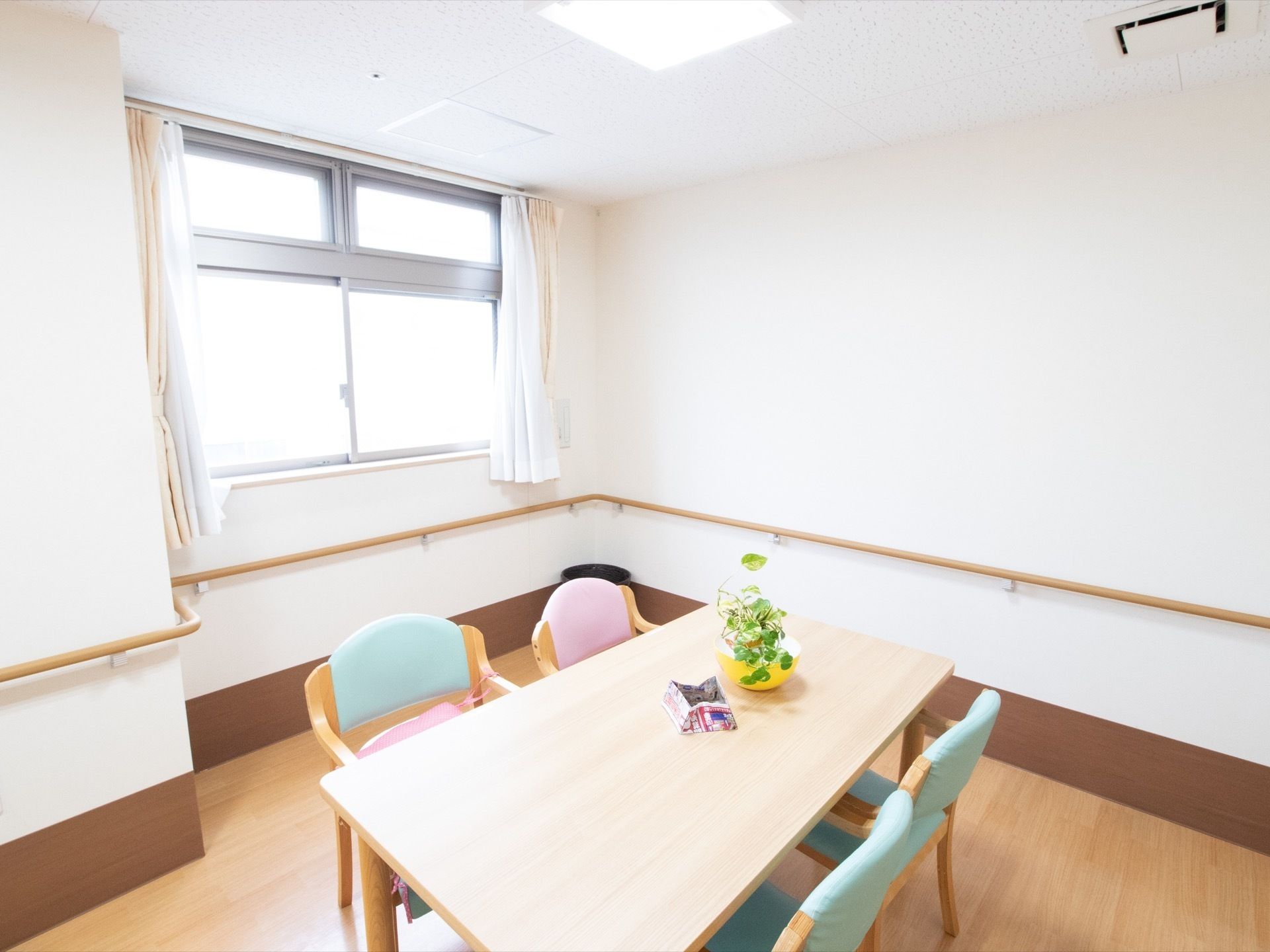 明るい広々した木製テーブル、ピンクとグリーンの椅子が備え付けられている。壁側には手すりが設置されている。