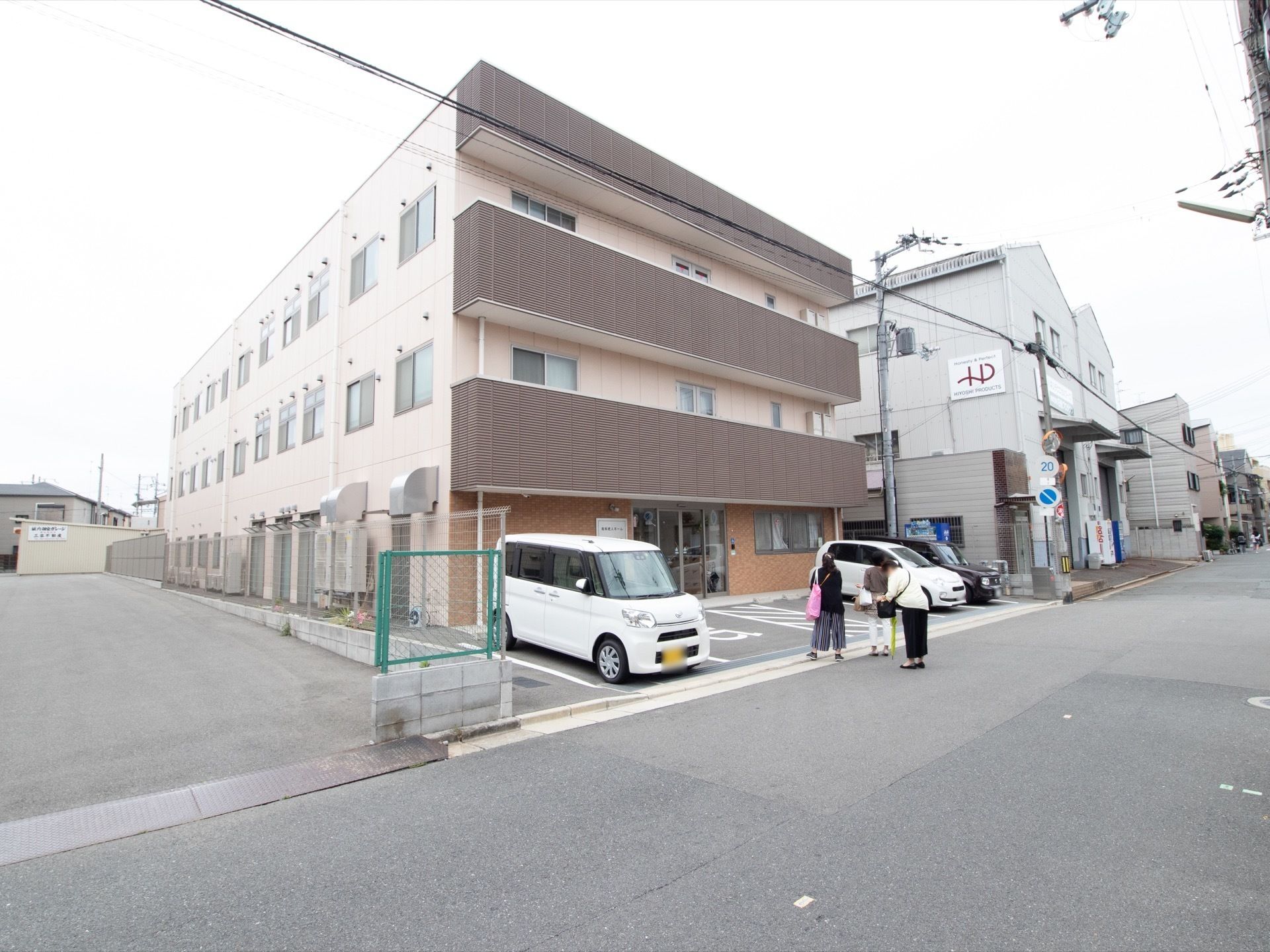 広大な敷地に建つ、住宅型の介護施設である。落ち着いた色合いでコーディネートされた外観。駐車場も完備されている。