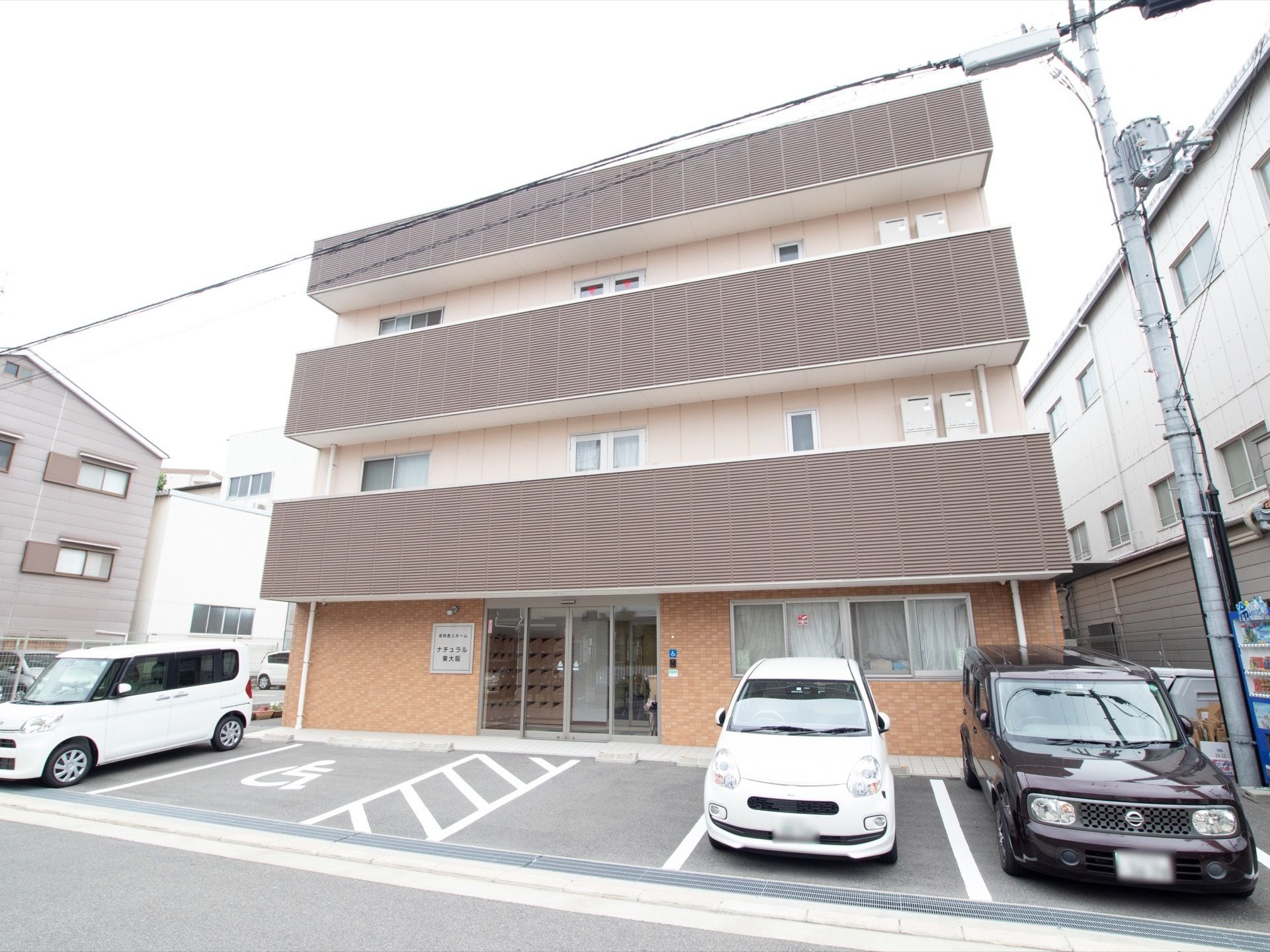 濃い茶色で施工されたベランダが印象的な、3階建ての施設である。玄関を出たところに、複数の駐車場が完備されている。