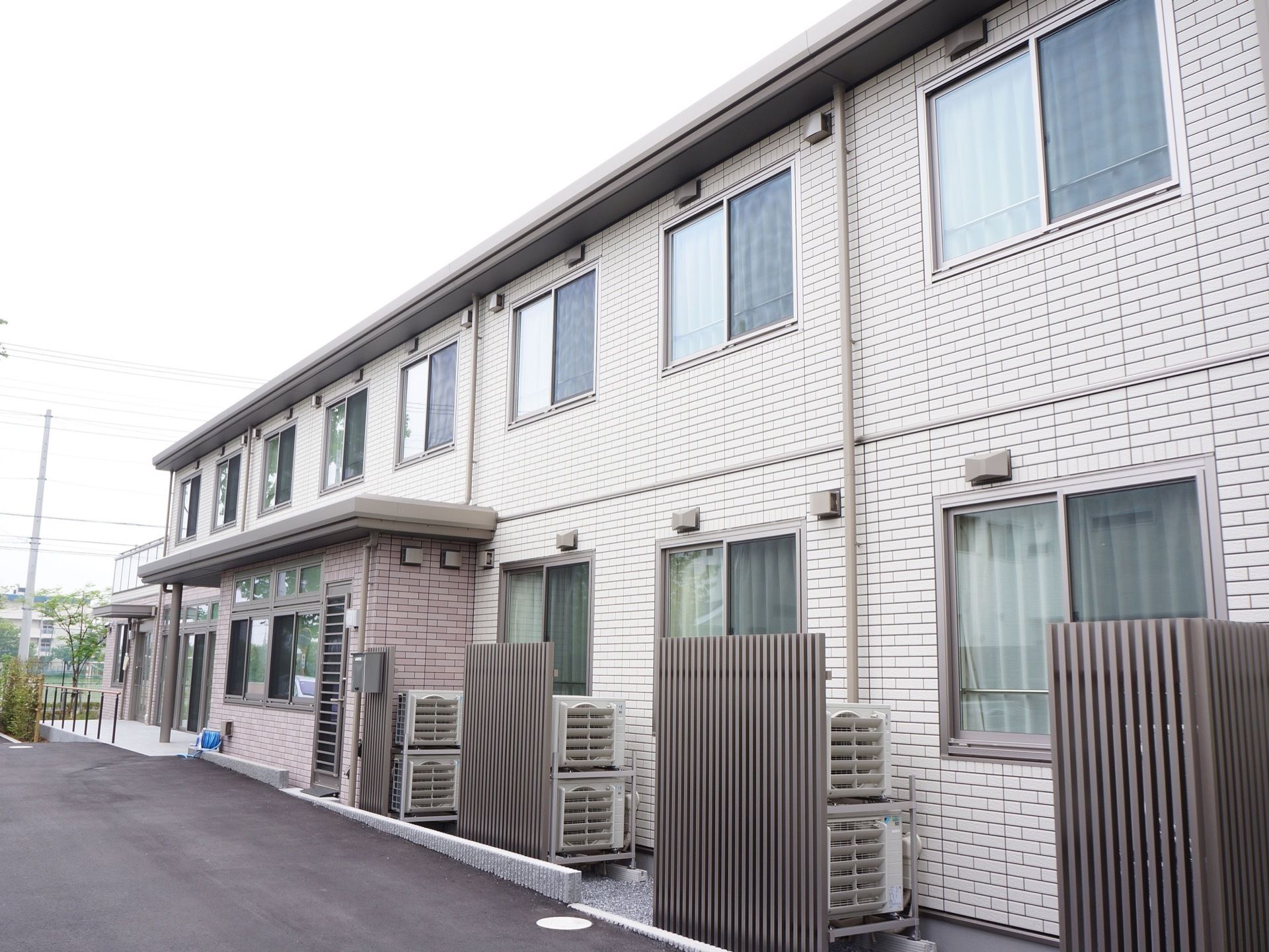 建物は２階建てで、全面が薄いグレーのレンガタイル貼りとなっている。各部屋の室外機は木製の柵で隠されている。