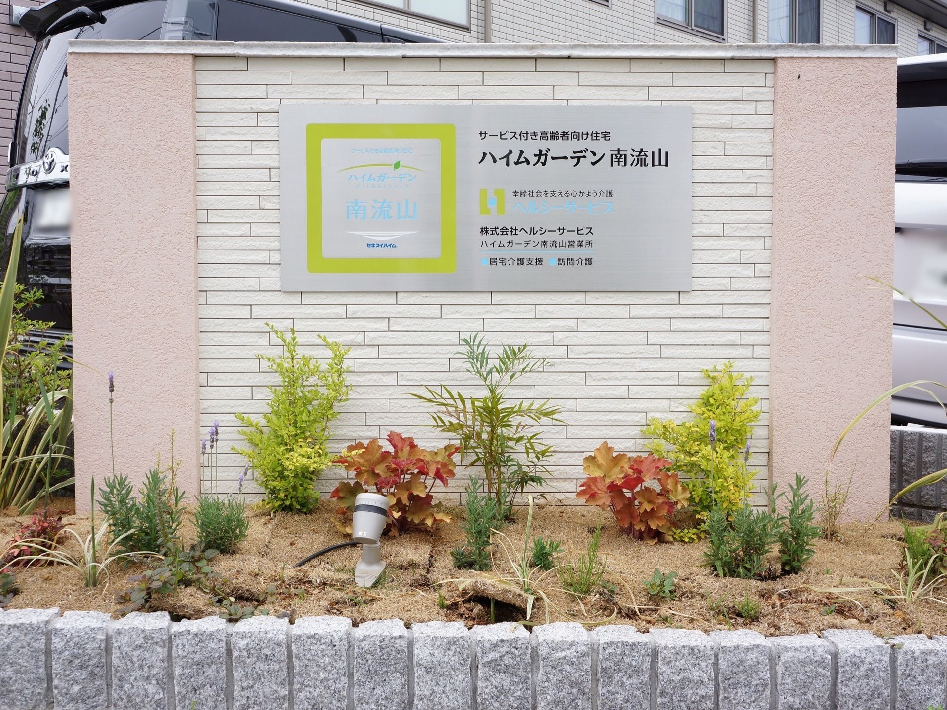 施設前には、施設名を表示した看板を設置している。看板周囲は植栽スペースを作り、季節の植物が来訪者様を出迎えている。