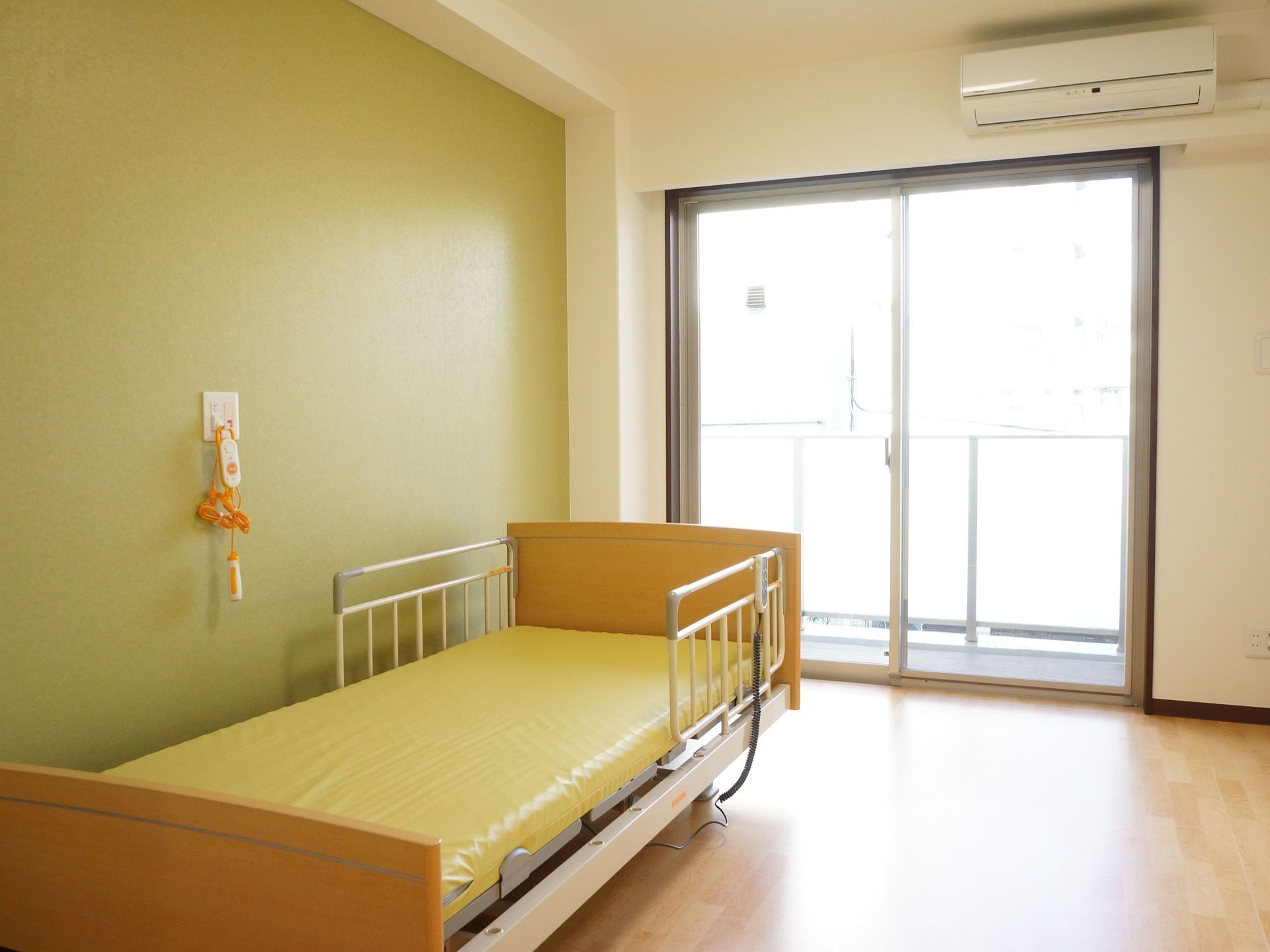 居室はベッド側の壁のみ明るいグリーンの壁紙が貼られており、モダンな印象である。エアコンと介護ベッド、緊急呼び出しボタンが備えられている。